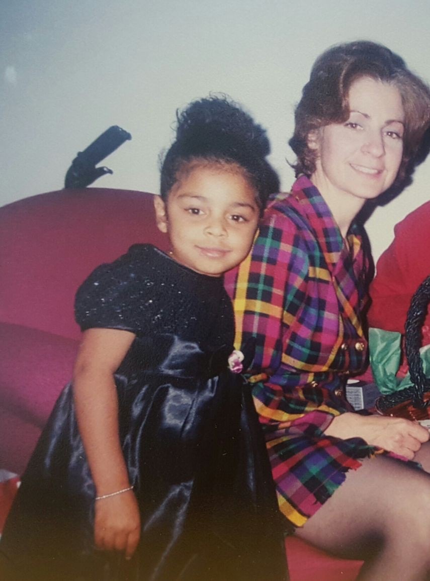 Two girls sitting on a red couch, smiling, one wearing a black dress and the other in a colorful plaid shirt.