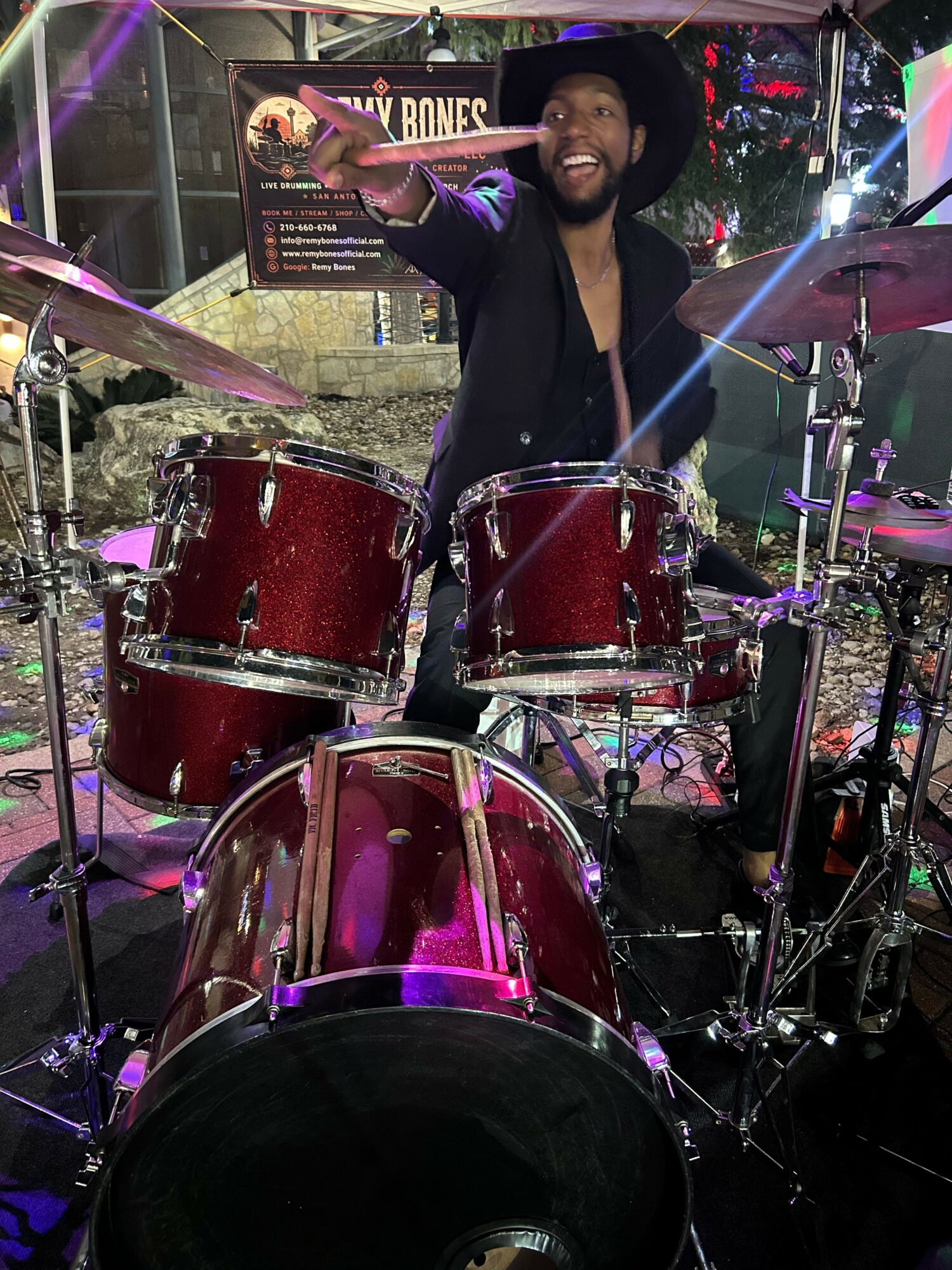 Person playing red drums on stage with colorful lights and equipment in background.
