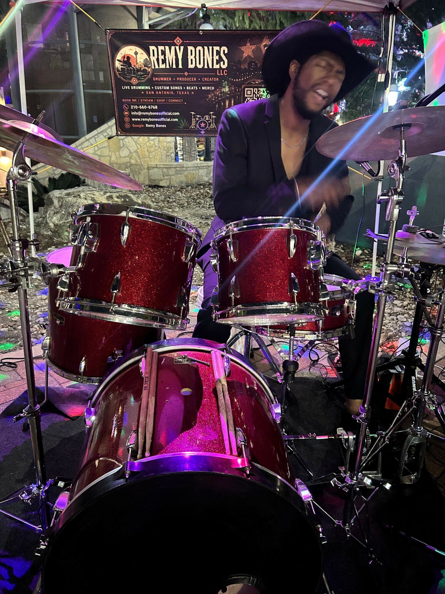 A woman playing a red drum set on stage with colorful lights and a sign in the background.