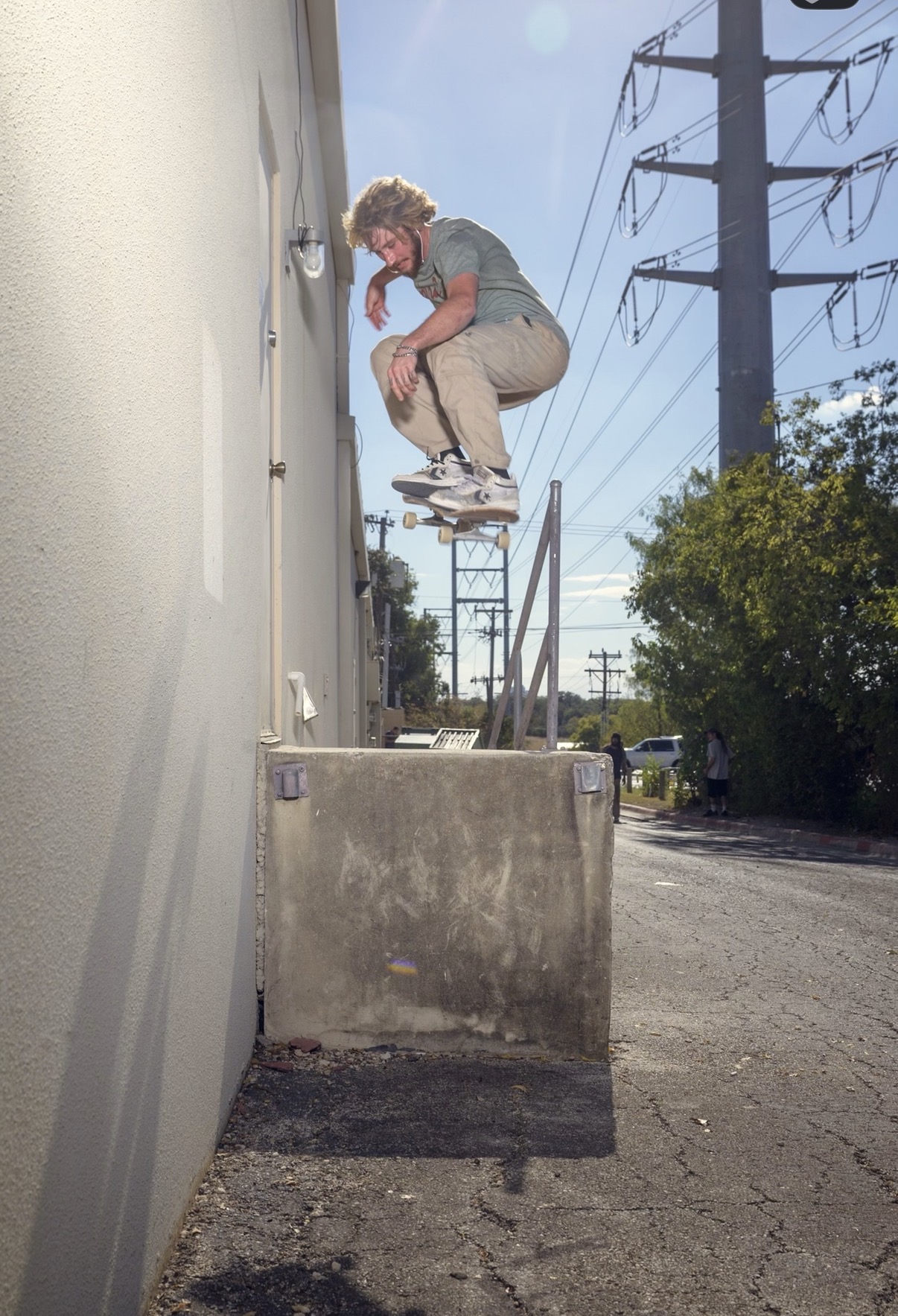 Person performing a skateboarding trick on a ledge outdoors, with power lines and trees in the background.