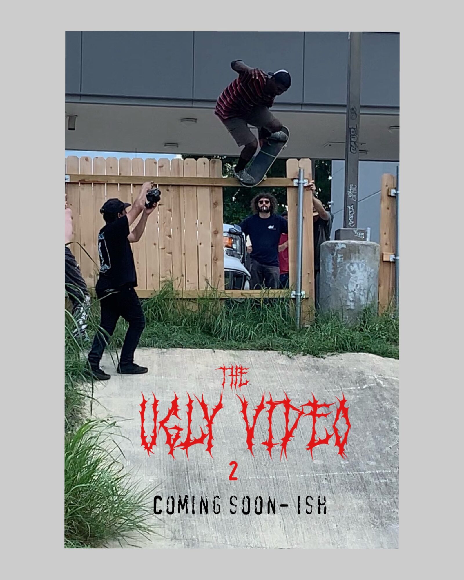 Person skateboarding over a fence with onlookers nearby, graffiti text reads 'The Ugly Viper 2 Coming Soon-ISH', grass and concrete visible.