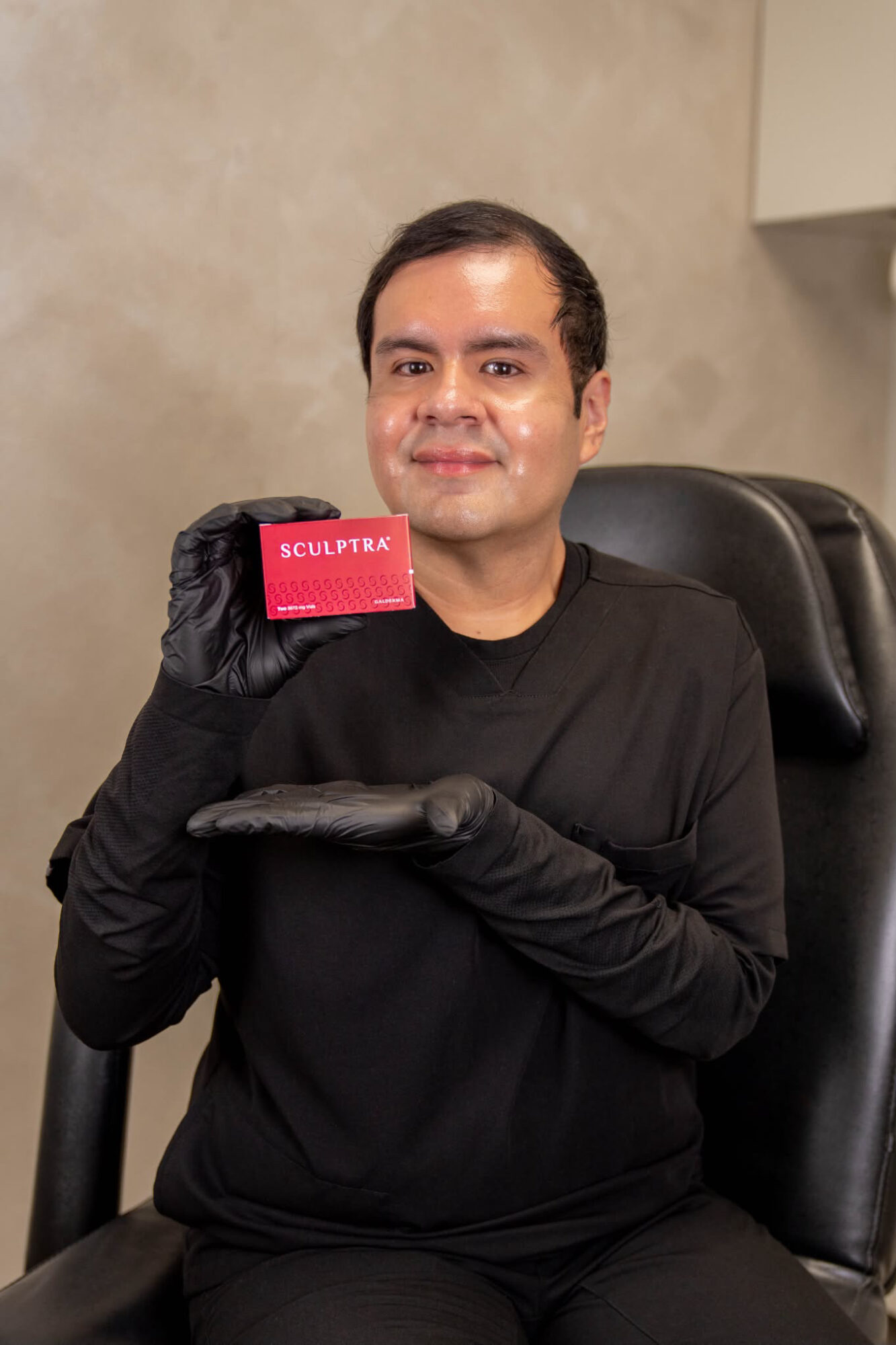 Person sitting in a chair holding a red card with white text, wearing black gloves and clothing, smiling.