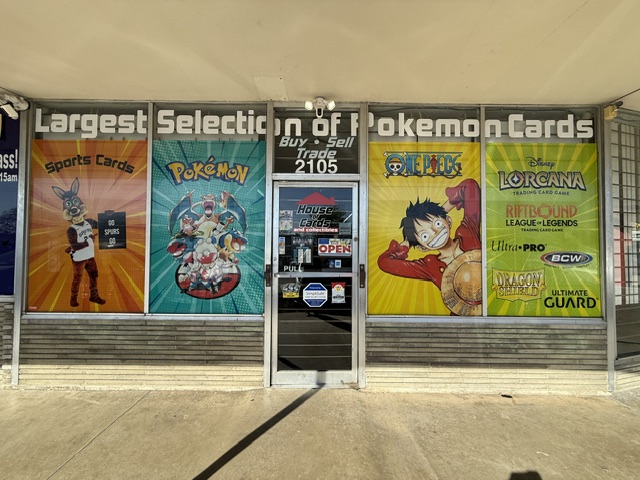 Storefront with Pokémon and trading card banners, glass door in the center, sunlight, and shadows on the ground.