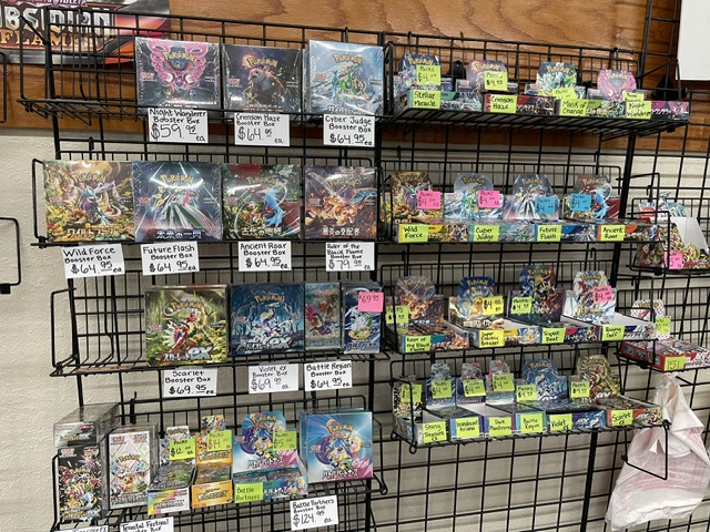 Display of various board games and card games on a black wire rack, with colorful packaging and price tags.