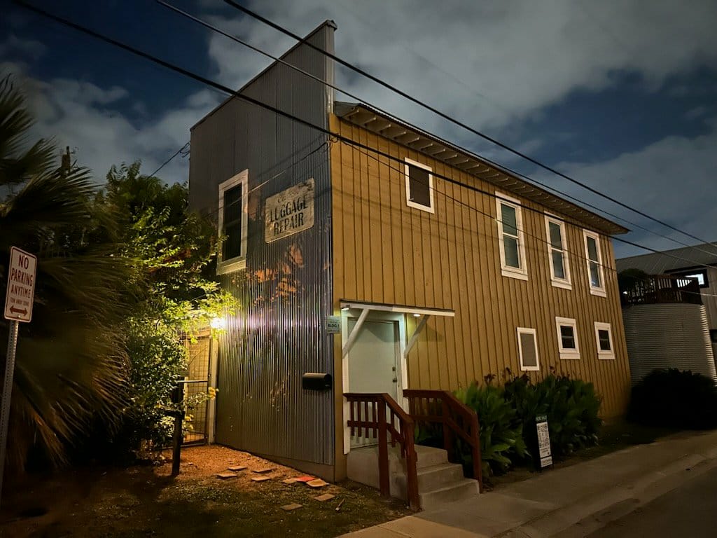 Two-story building with vertical siding, multiple windows, and a small staircase leading to the entrance, illuminated at dusk.