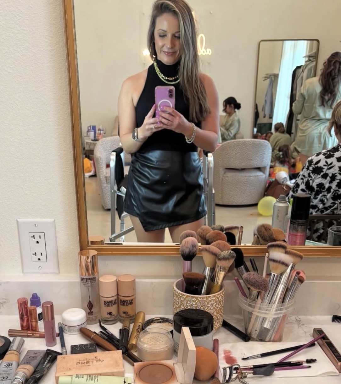 Woman taking a mirror selfie in a room with makeup and beauty products on the counter.