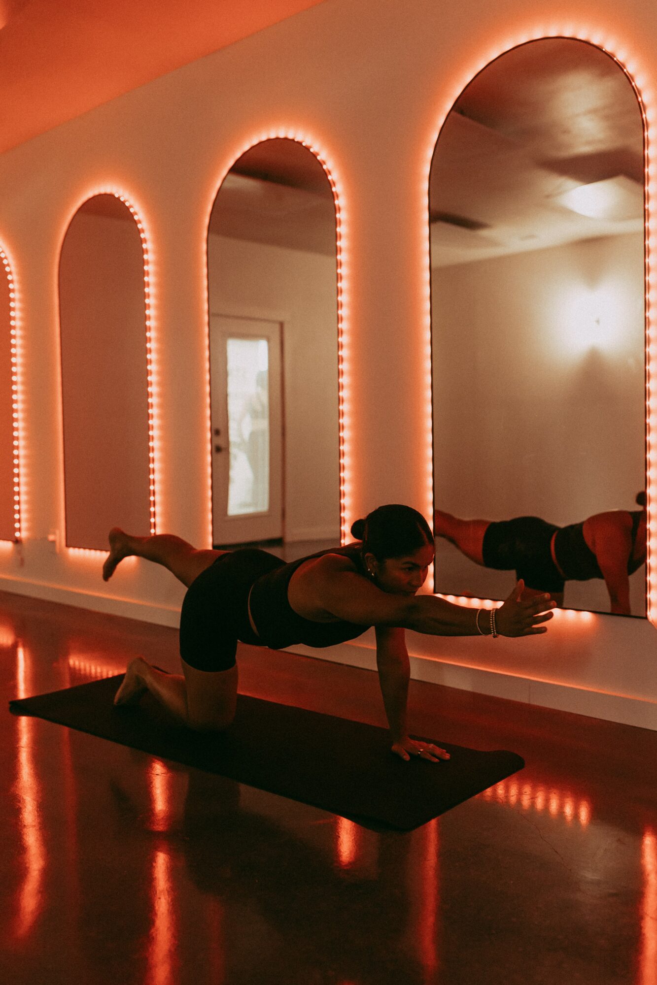 Person practicing yoga on a mat in a dimly lit room with arched windows and warm lighting.
