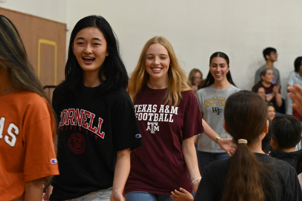Group of smiling young women in casual clothing at an indoor event, some with long hair, others with short hair.