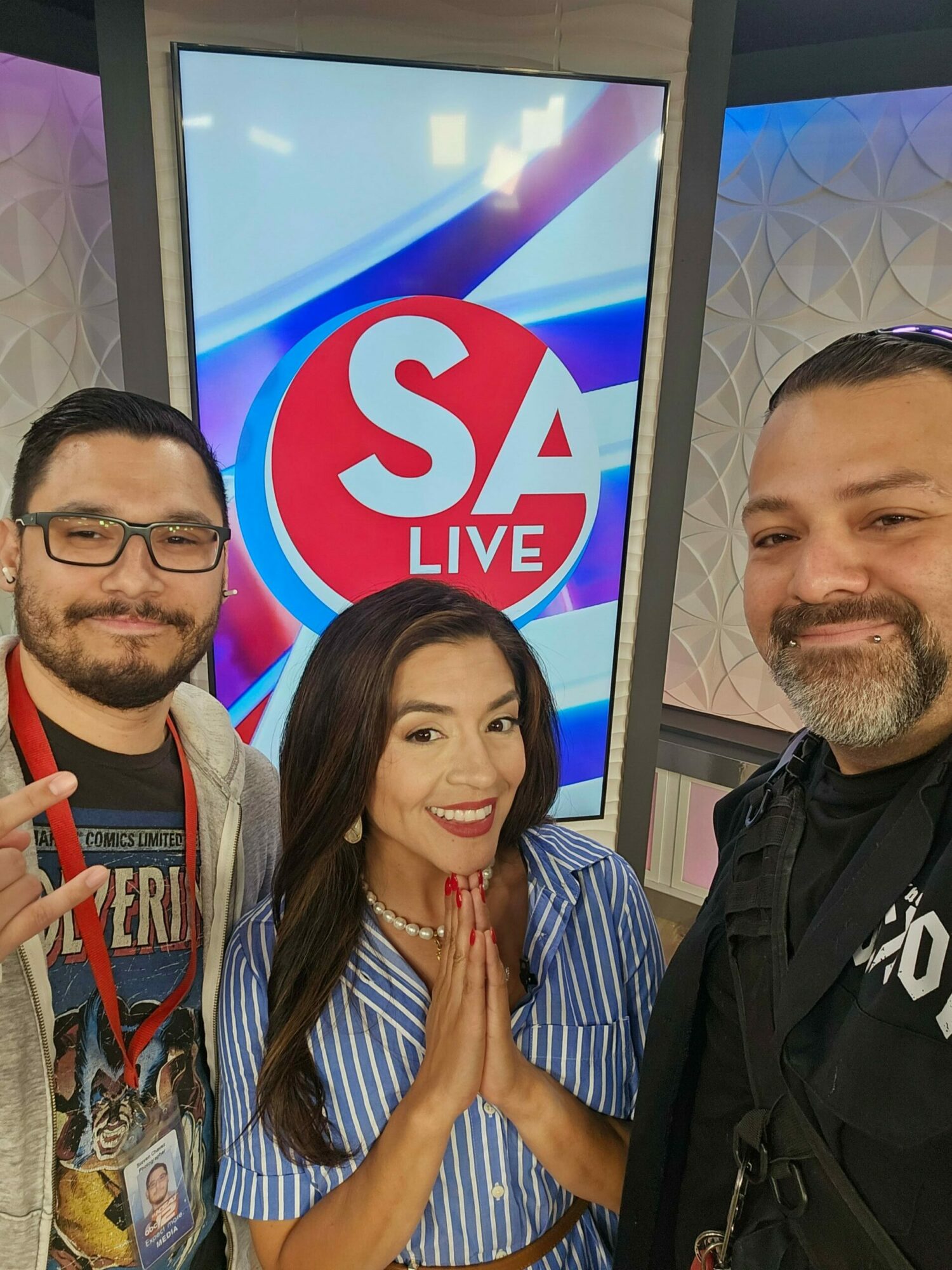 Three people smiling in front of a TV screen with a red and blue logo, two women and one man, indoors.