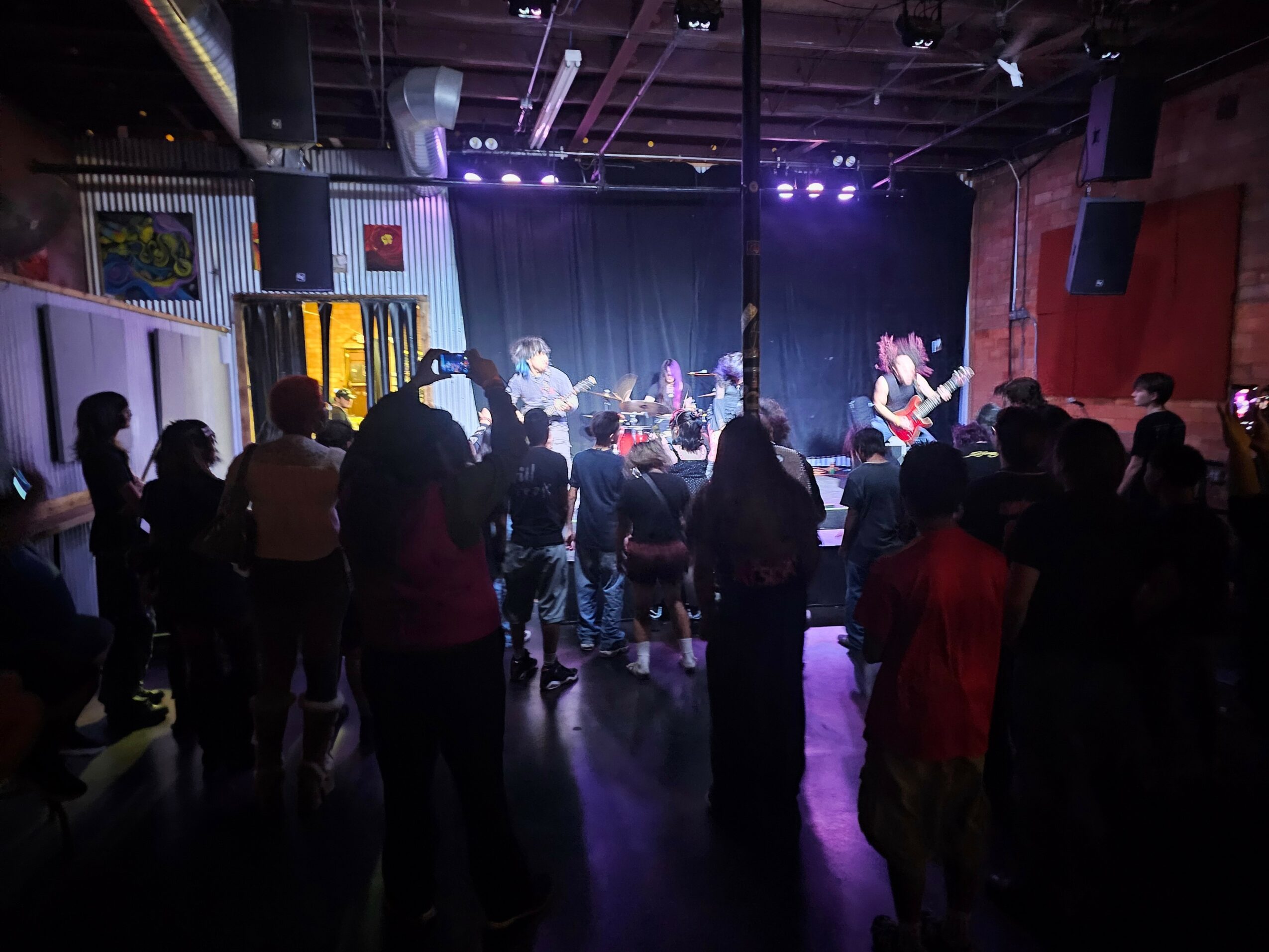 People watching a live band perform on stage in a dimly lit venue with purple lighting.