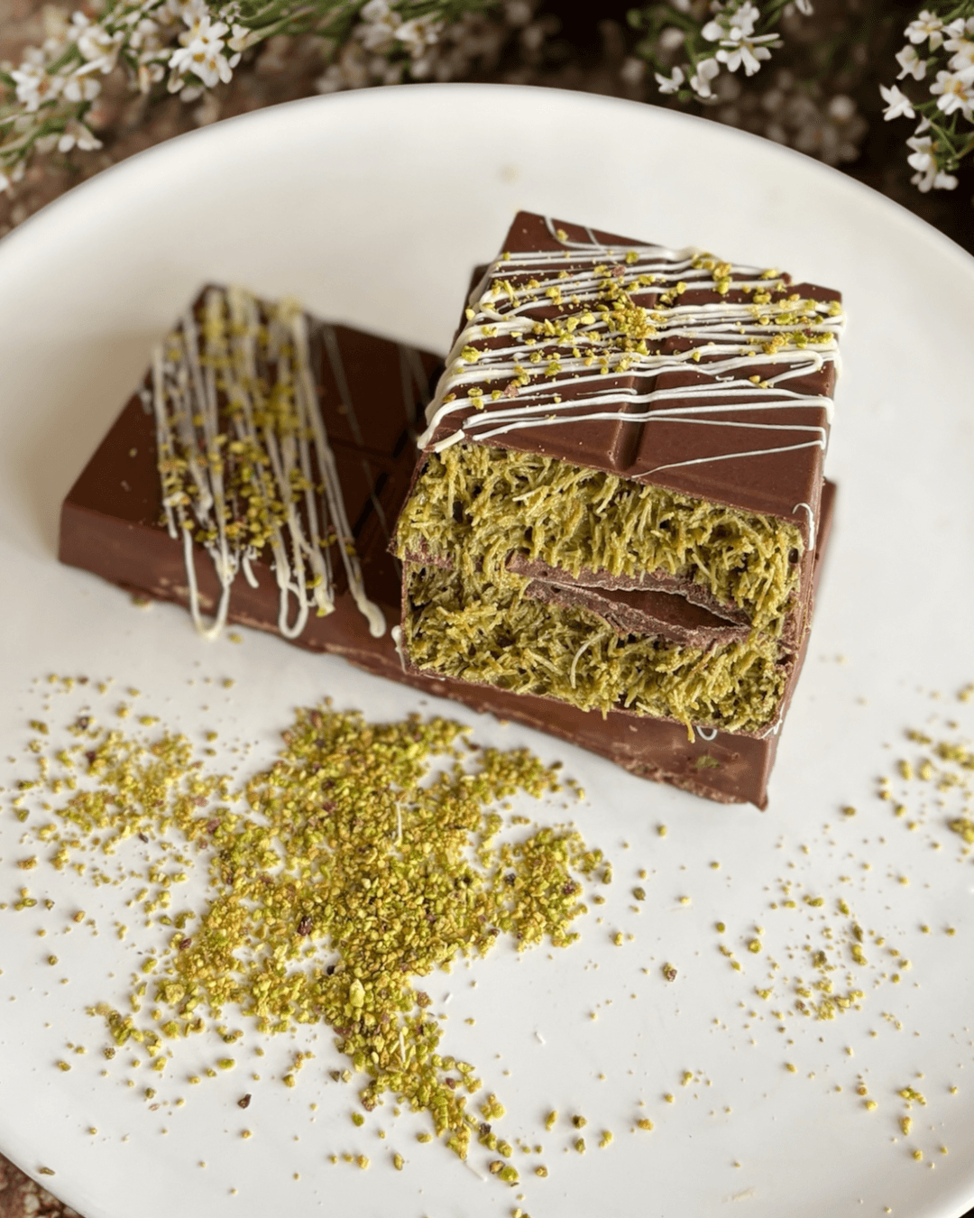 Piece of layered cake with chocolate and green filling, decorated with white and yellow drizzle, on a white plate with green sprinkles.
