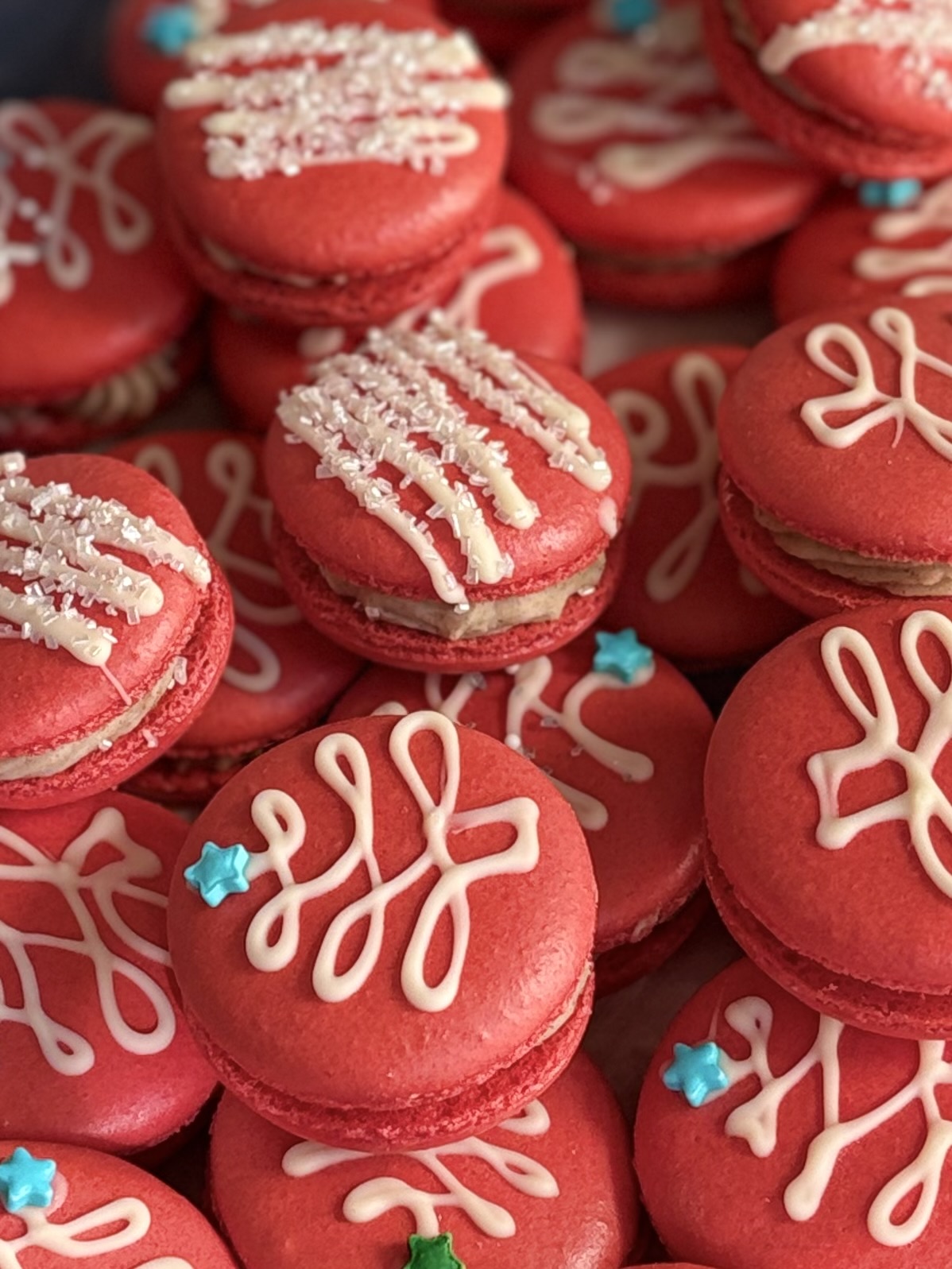 Red macarons decorated with white icing and small blue star-shaped sprinkles, arranged closely together.