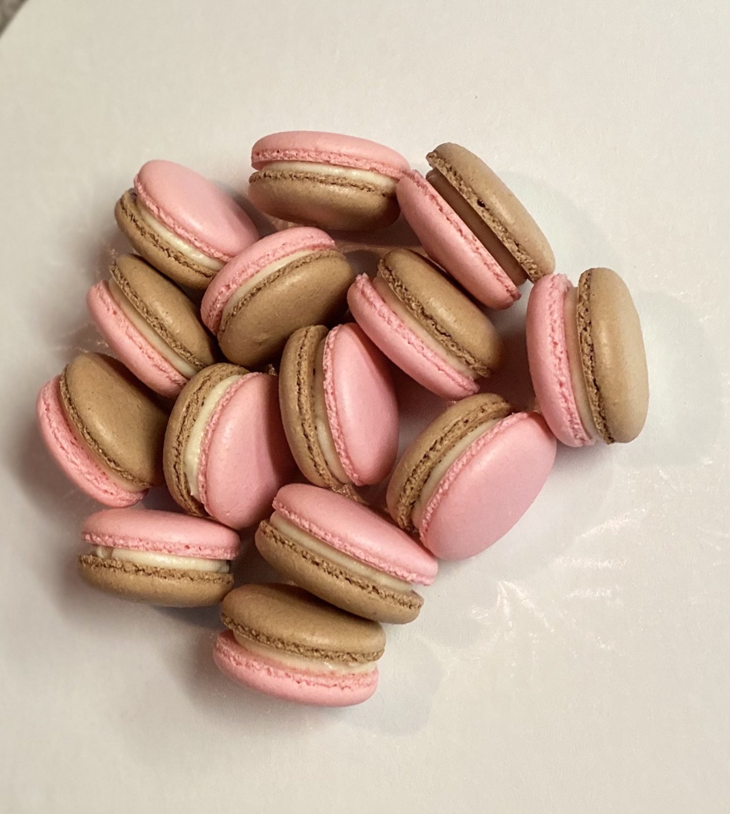 Pink and brown macarons scattered on a white surface, some overlapping each other.