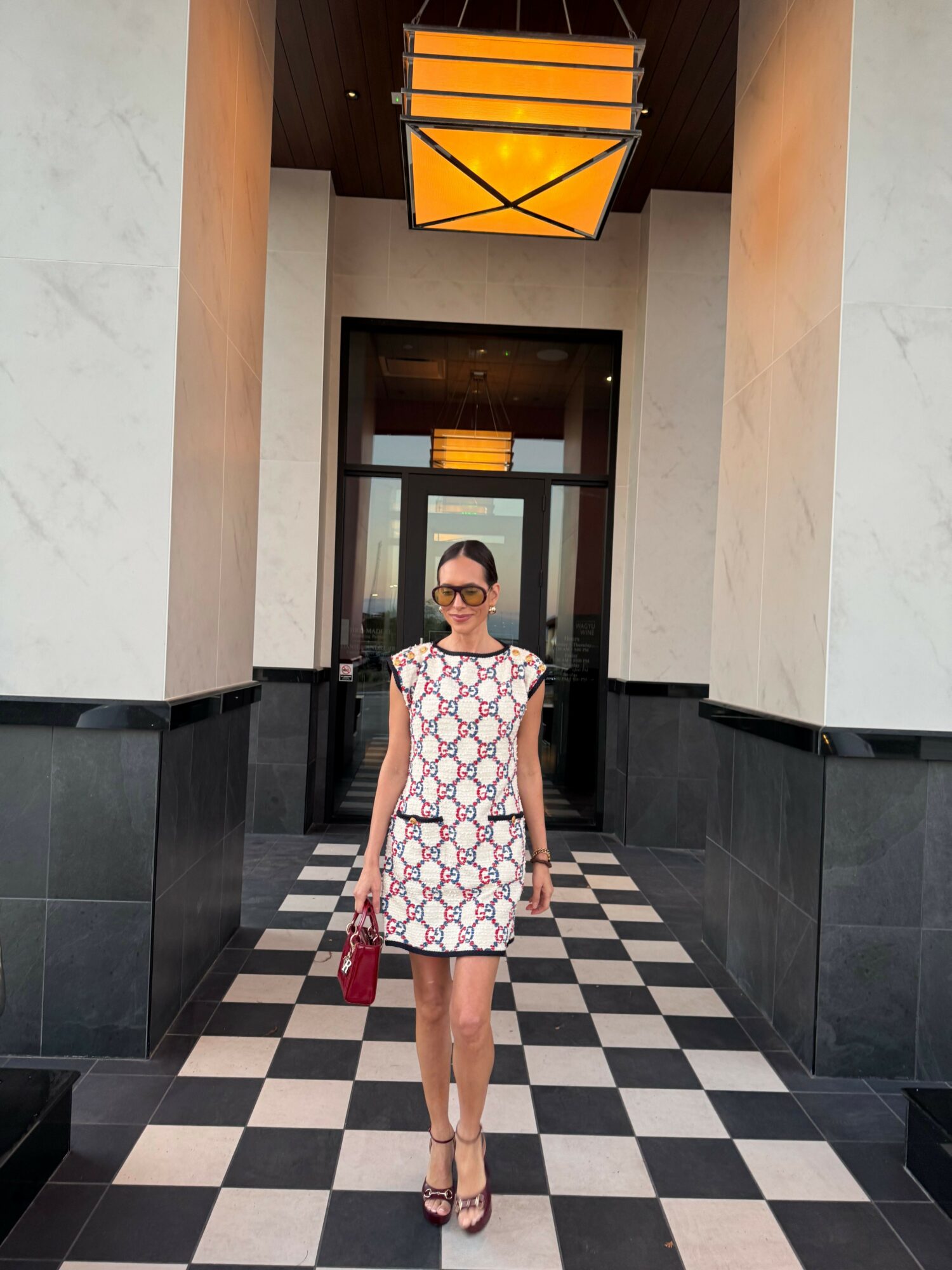 Woman in patterned dress standing in hallway with checkered floor and modern decor.
