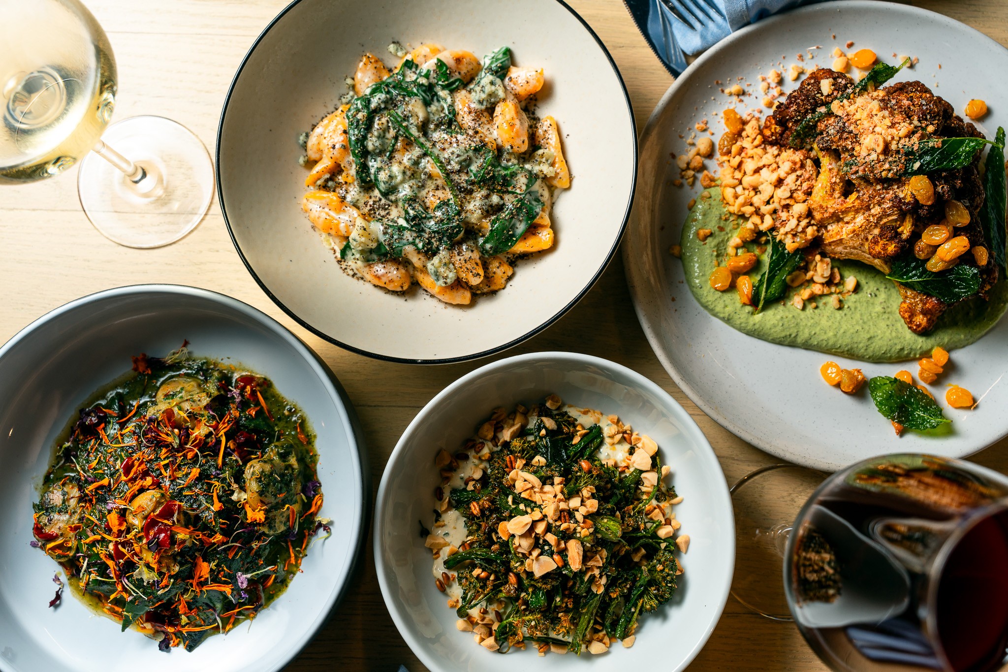 Four plates of food with a glass of white wine and a glass of red wine on a table, top view