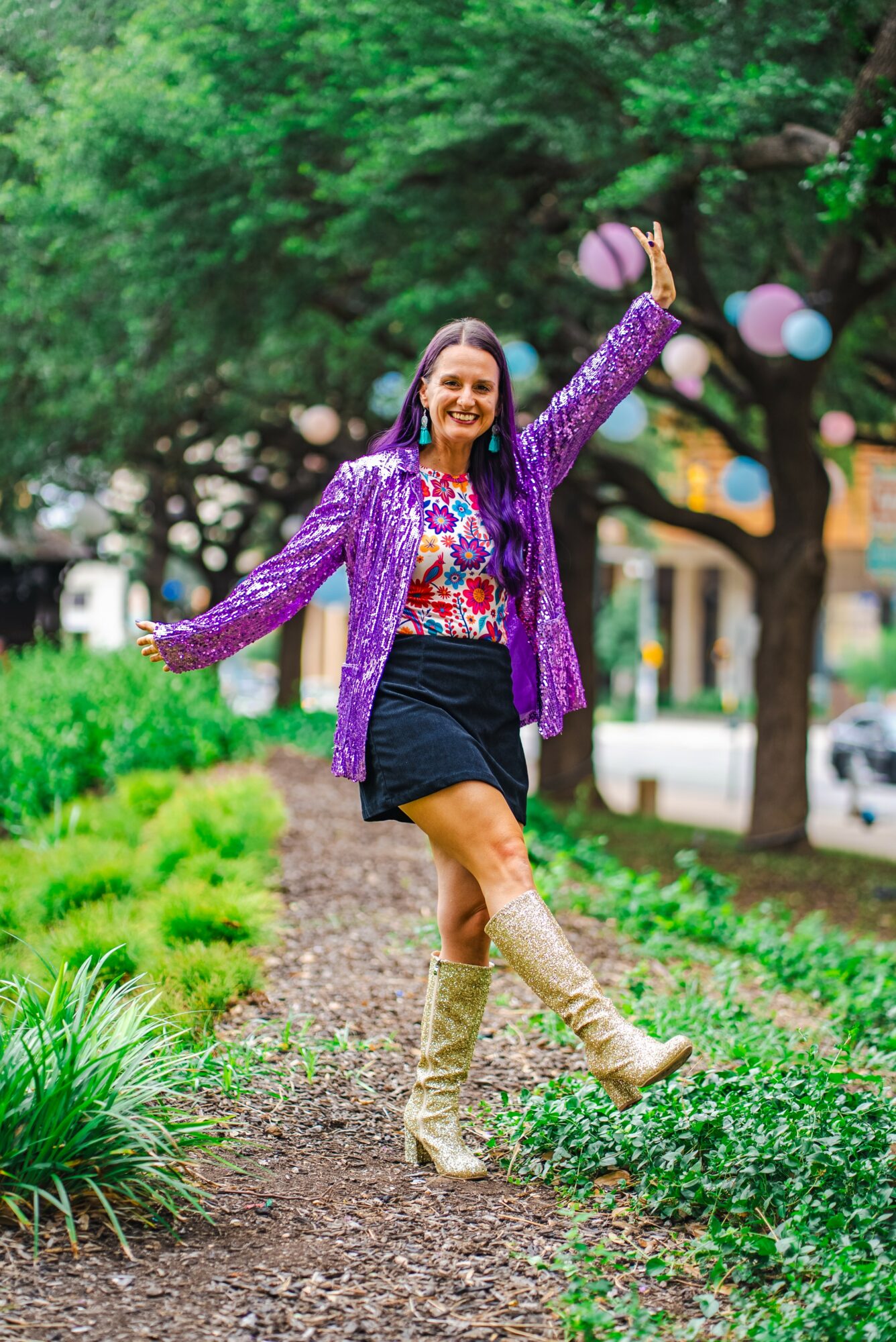 Woman in colorful outfit dancing outdoors with trees and lanterns in background.