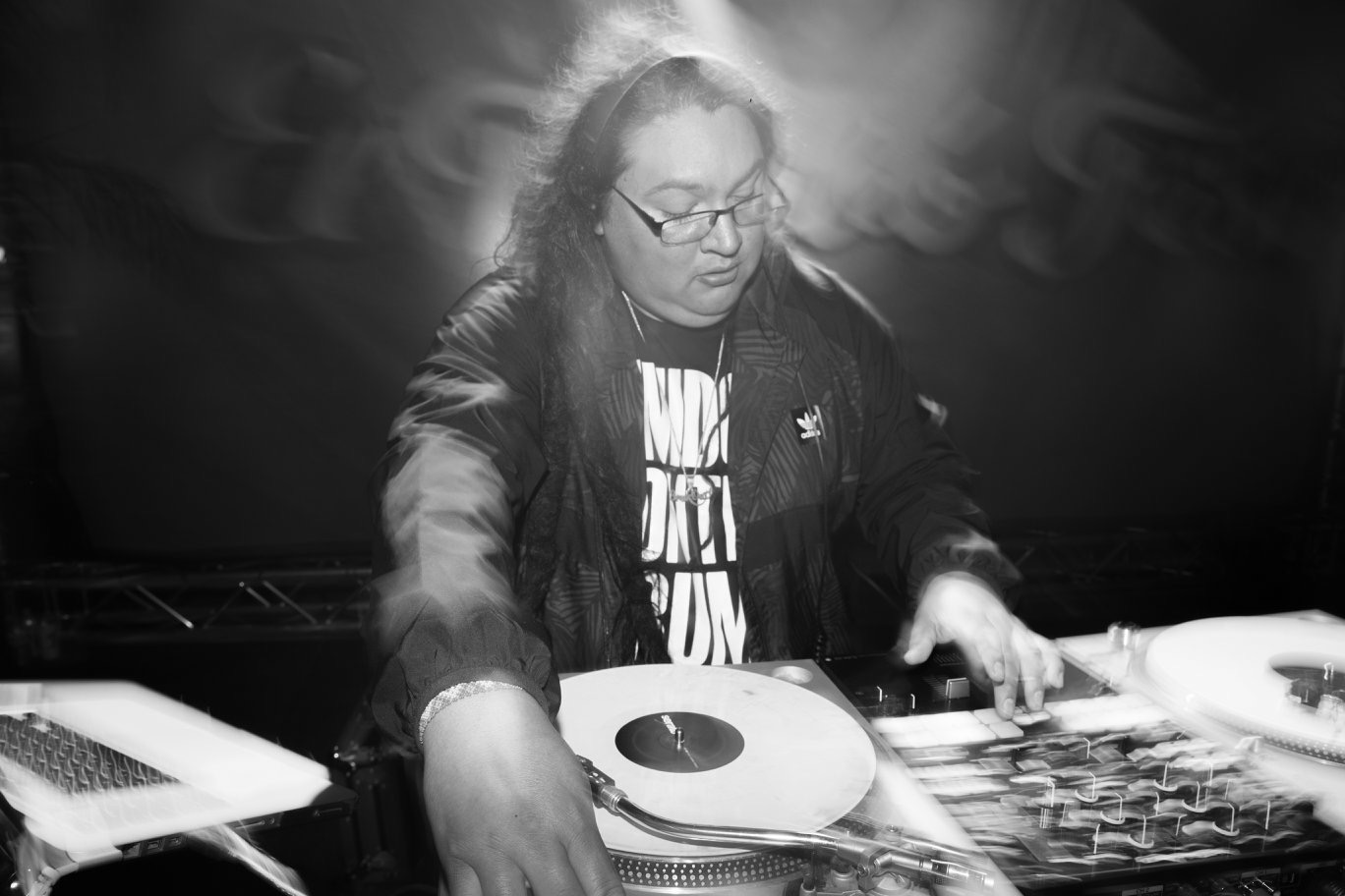 Woman with glasses and long hair working at a table with electronic equipment, in black and white.