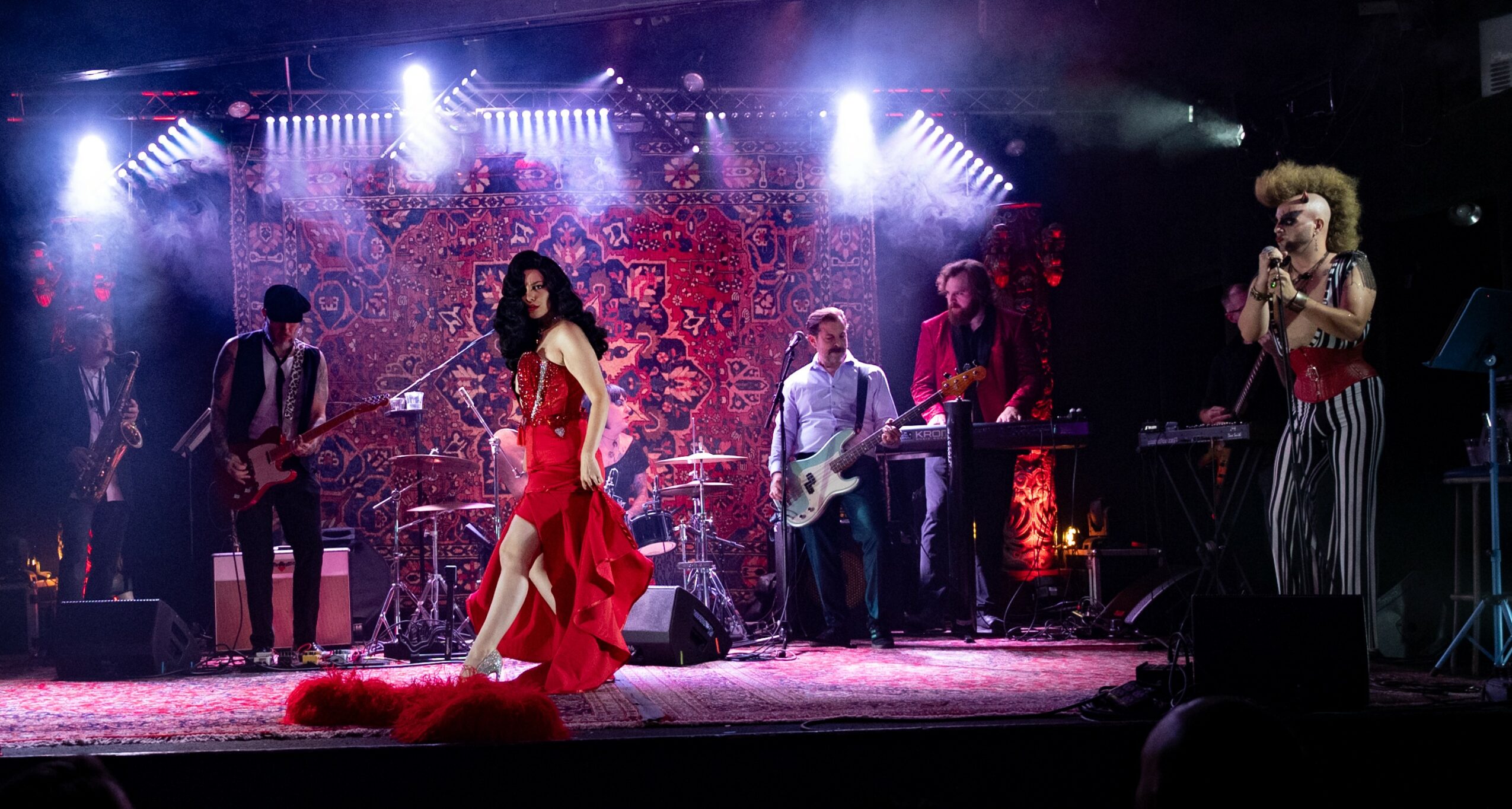 Musicians and a singer perform on stage with colorful lighting and a decorative backdrop.
