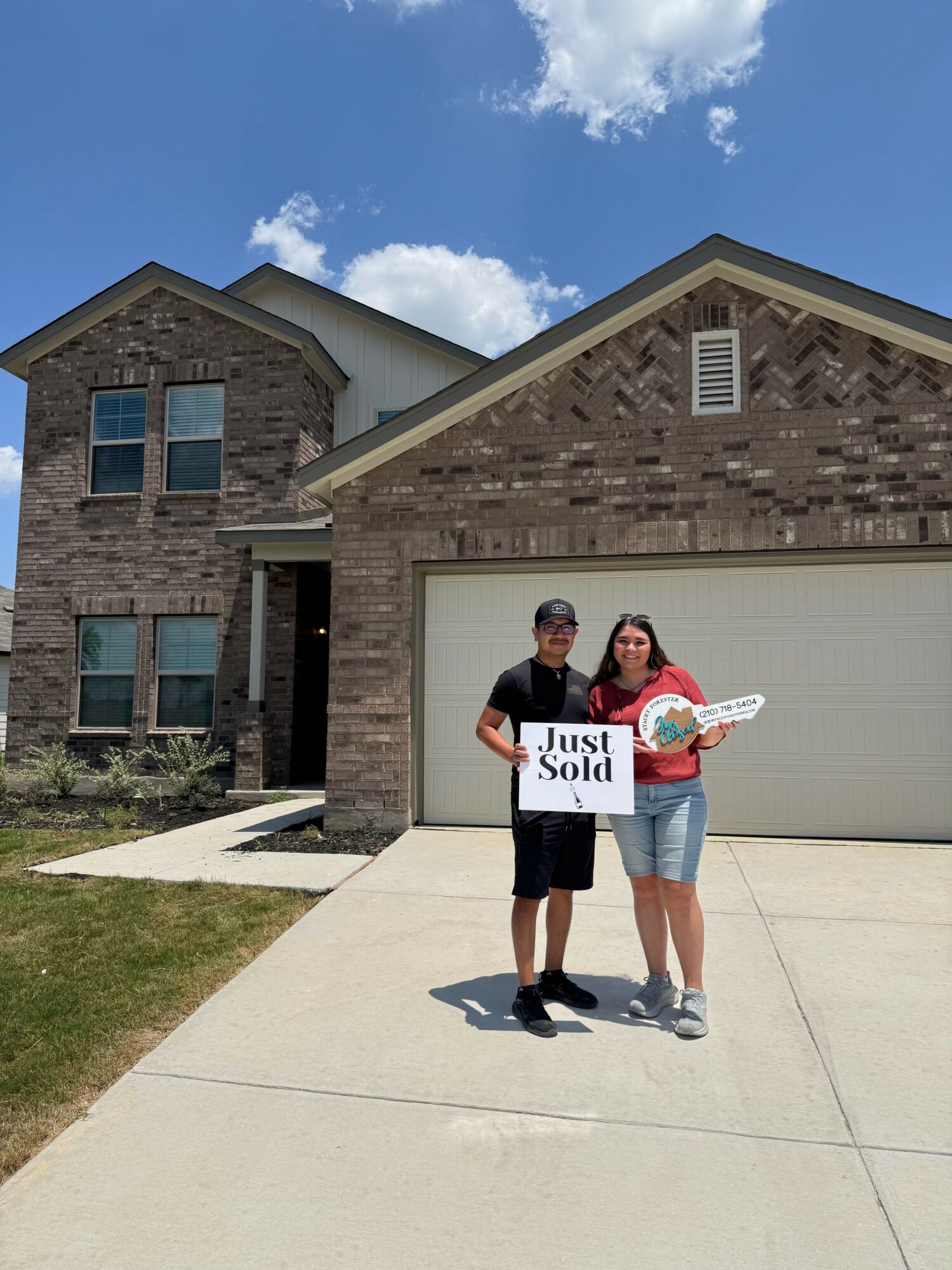 Two people standing outside a building holding signs, one with a large white sign and the other with a smaller sign, on a sunny day.