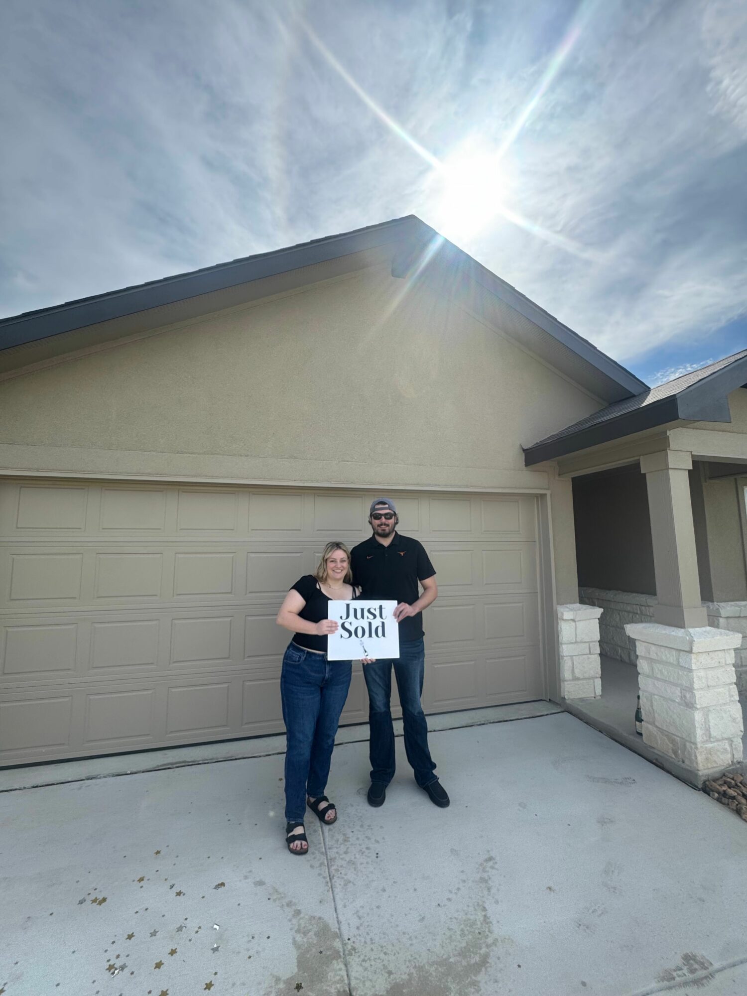 Two people standing outside a garage, one holding a sign, with a partly cloudy sky above.
