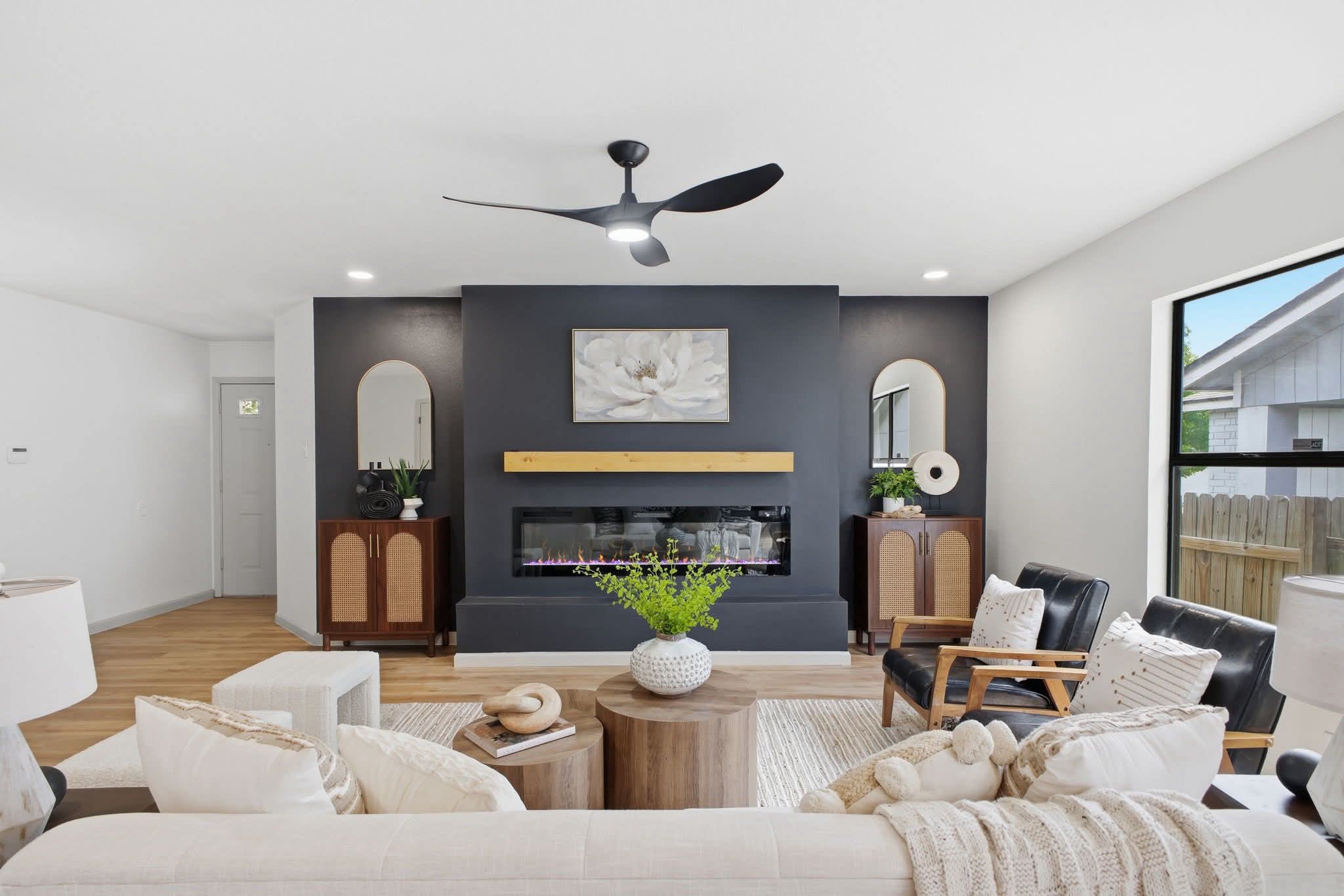 Living room with a fireplace, dark accent wall, and large window, furnished with sofas, chairs, and a coffee table.