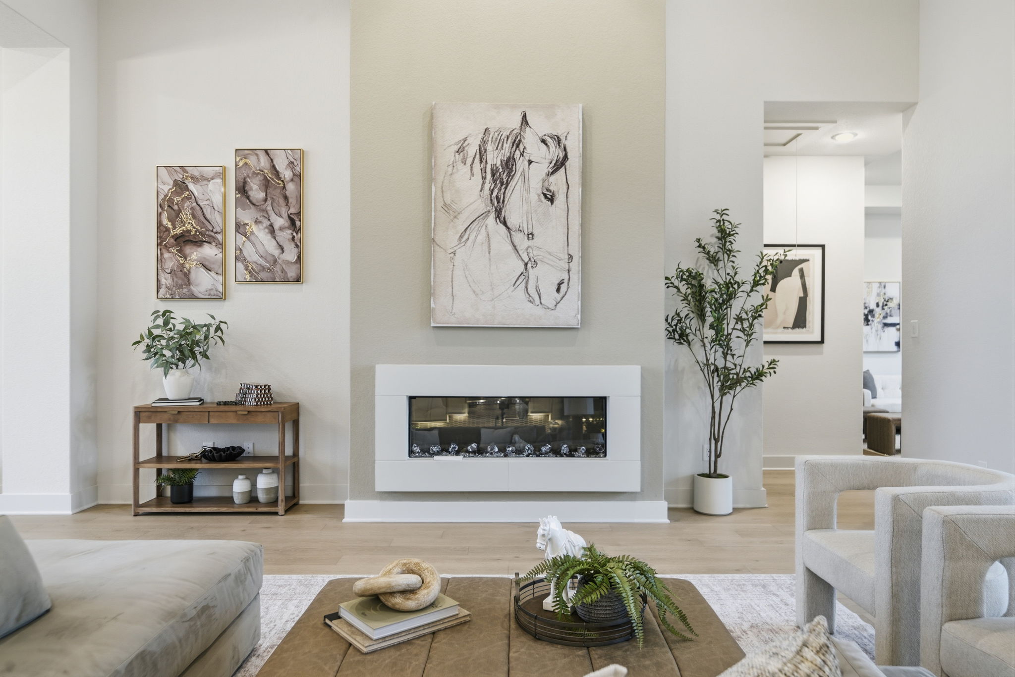 Living room with artwork, fireplace, plants, and furniture, bright and modern decor, light-colored walls and wooden flooring.