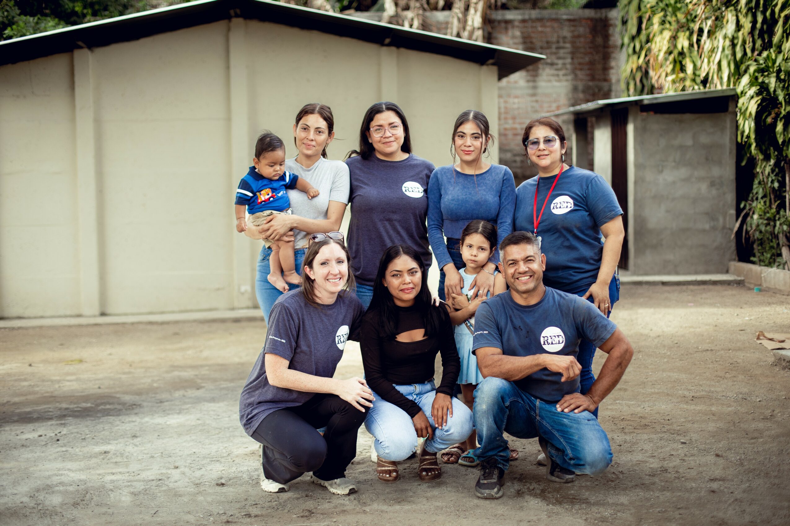 Group of eight people, including children, standing outdoors in front of a building, smiling at the camera.