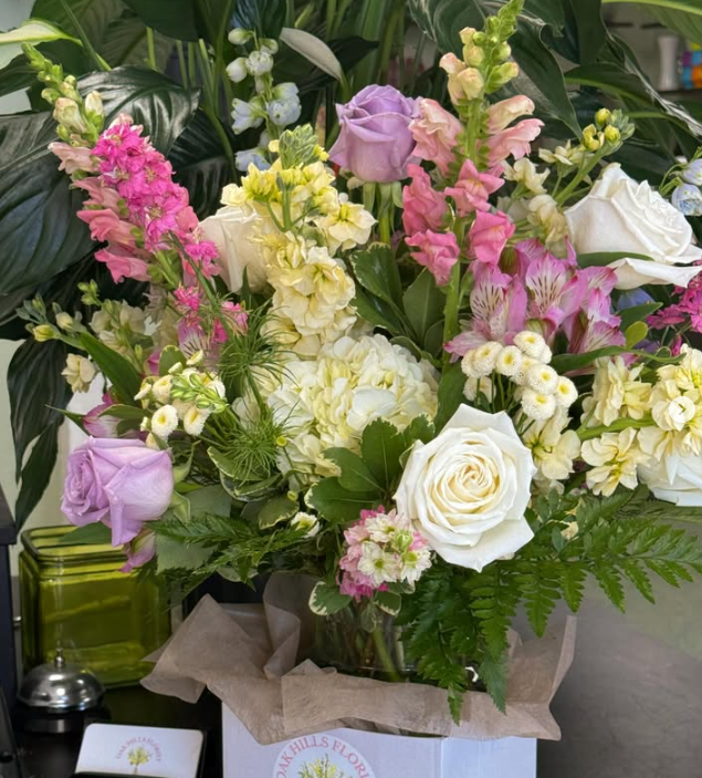 A colorful bouquet of various flowers including roses, snapdragons, and other blooms with green foliage, arranged in a vase.