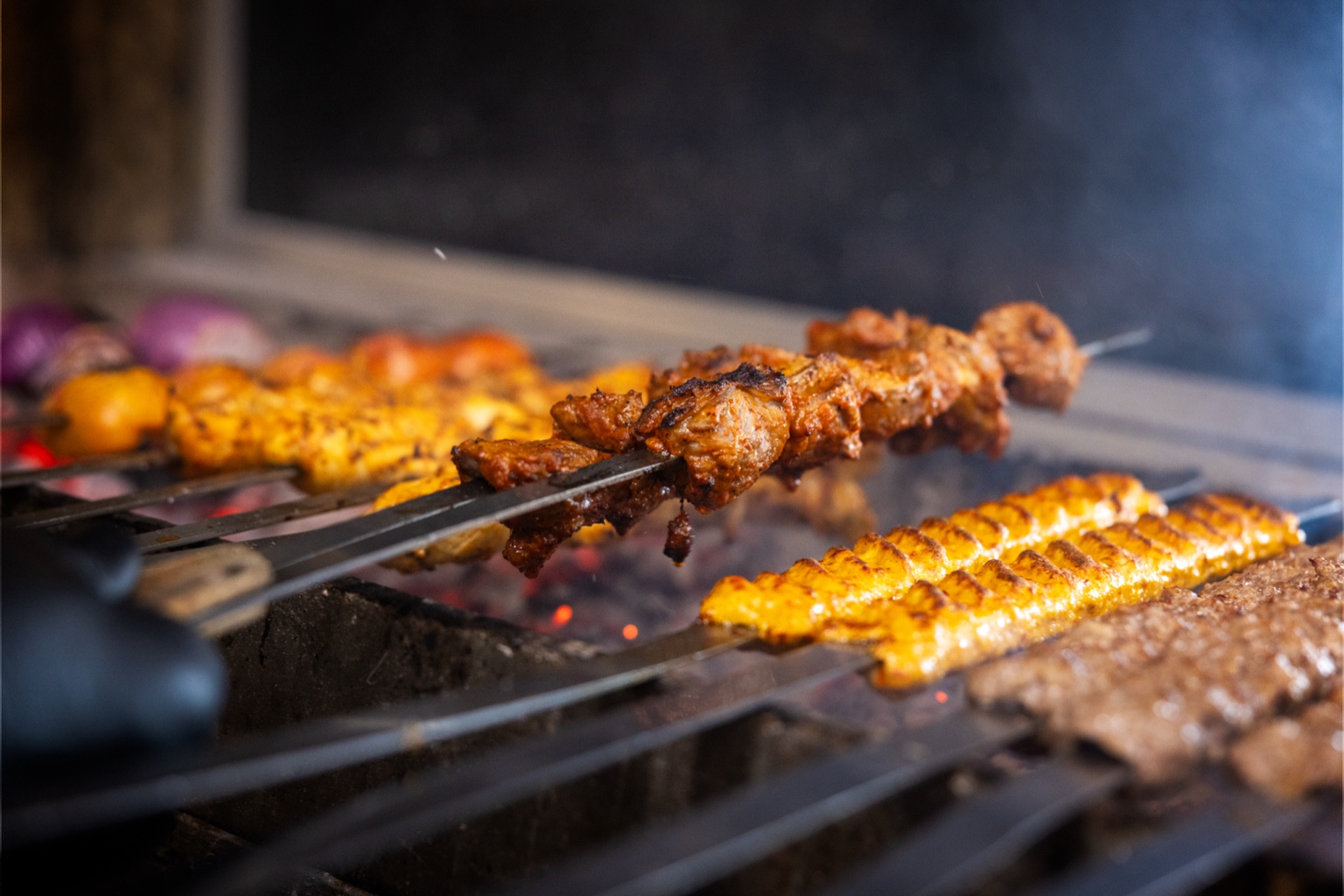 Meat and vegetables grilling on a barbecue with smoke, skewers, and corn on the grill.
