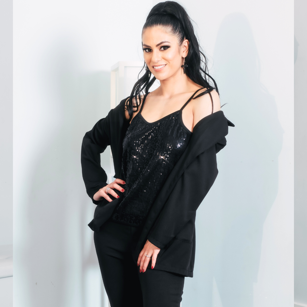 Woman with long dark hair in a high ponytail, wearing a black sequined top and black jacket, smiling confidently.