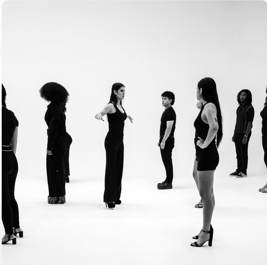 Group of people standing in a circle, facing each other, in a white studio space.