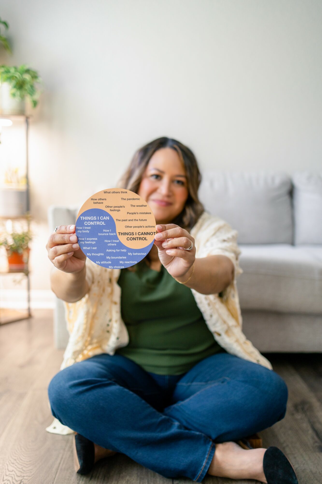 Woman sitting on the floor holding a circular chart, smiling, in a living room with a sofa and plants.