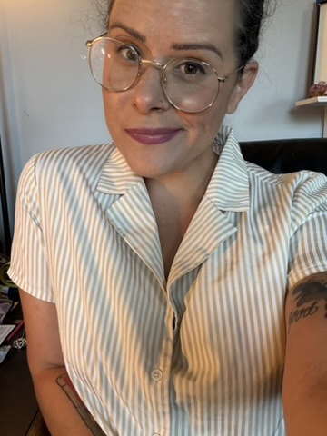 Woman with glasses and dark hair in a striped shirt, smiling, indoors.