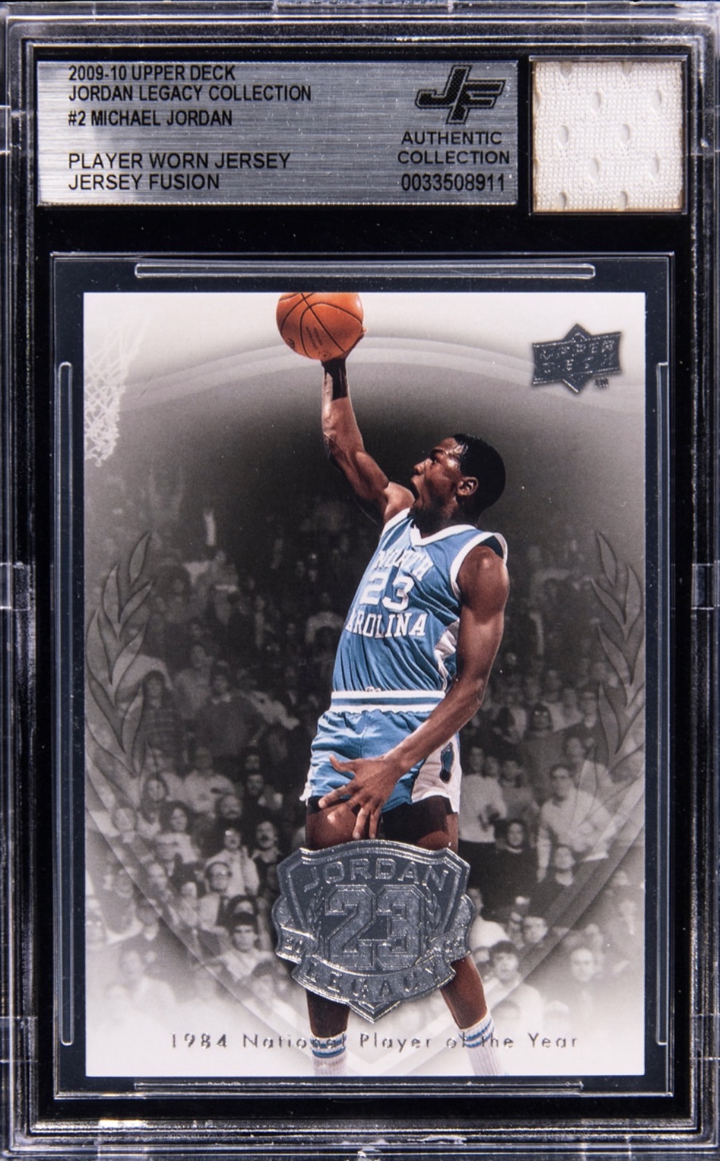 Basketball player in blue uniform jumping with a ball, holding a trophy, with a crowd in the background.