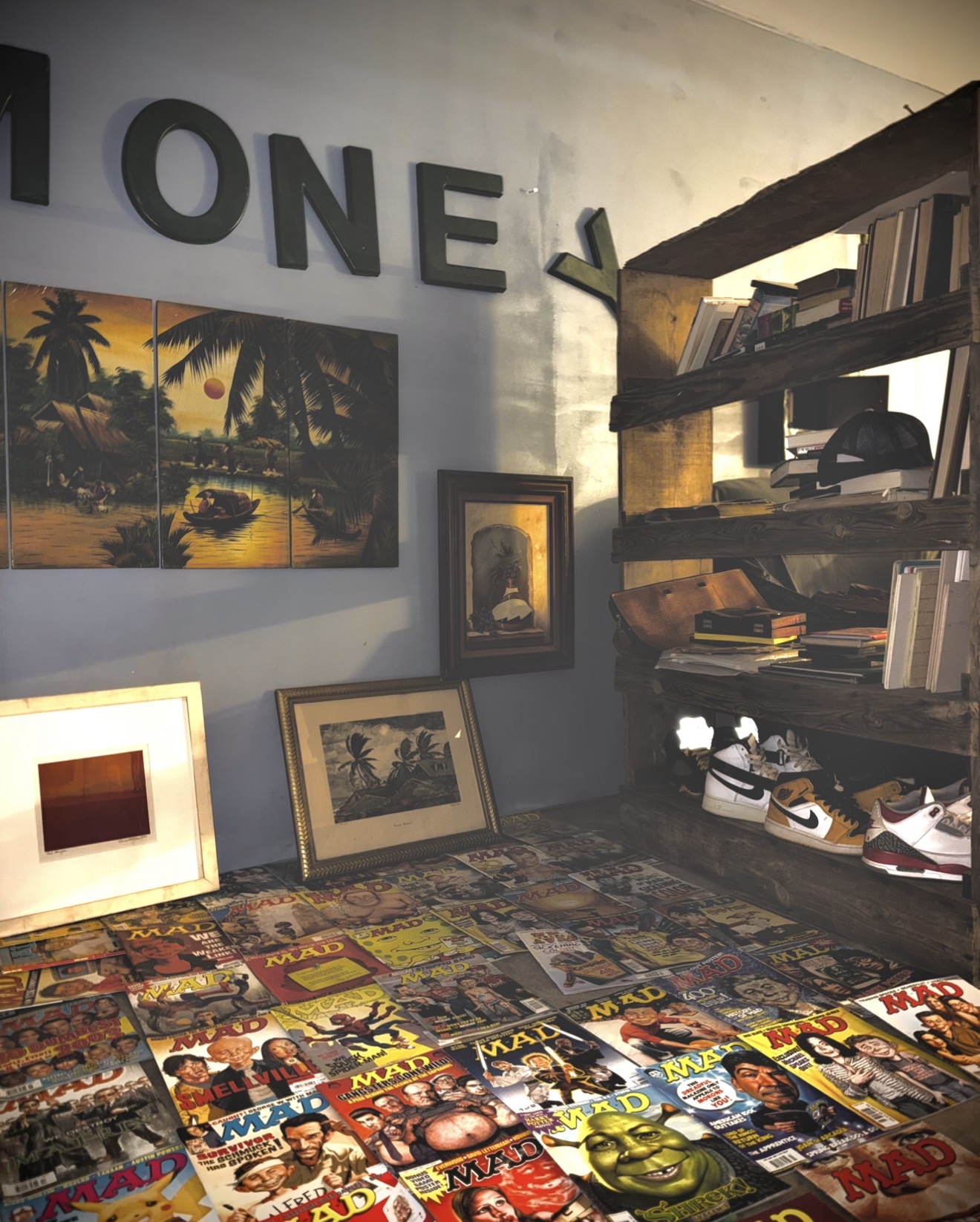 Books and magazines on a table, framed pictures on the wall, and a wooden shelf with books and objects.