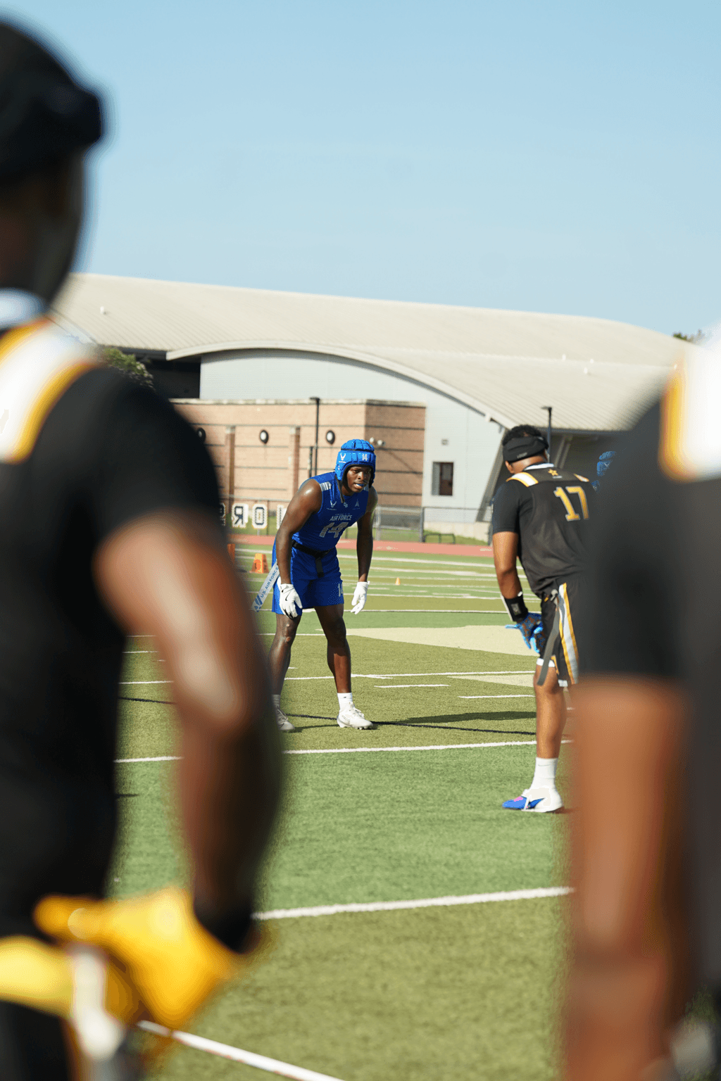 Football players on field during practice, with a clear blue sky in background.