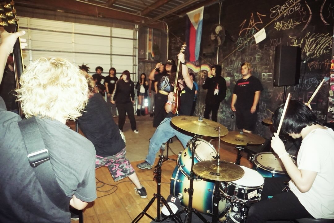 People dancing and playing drums in a lively indoor space with graffiti on the wall.