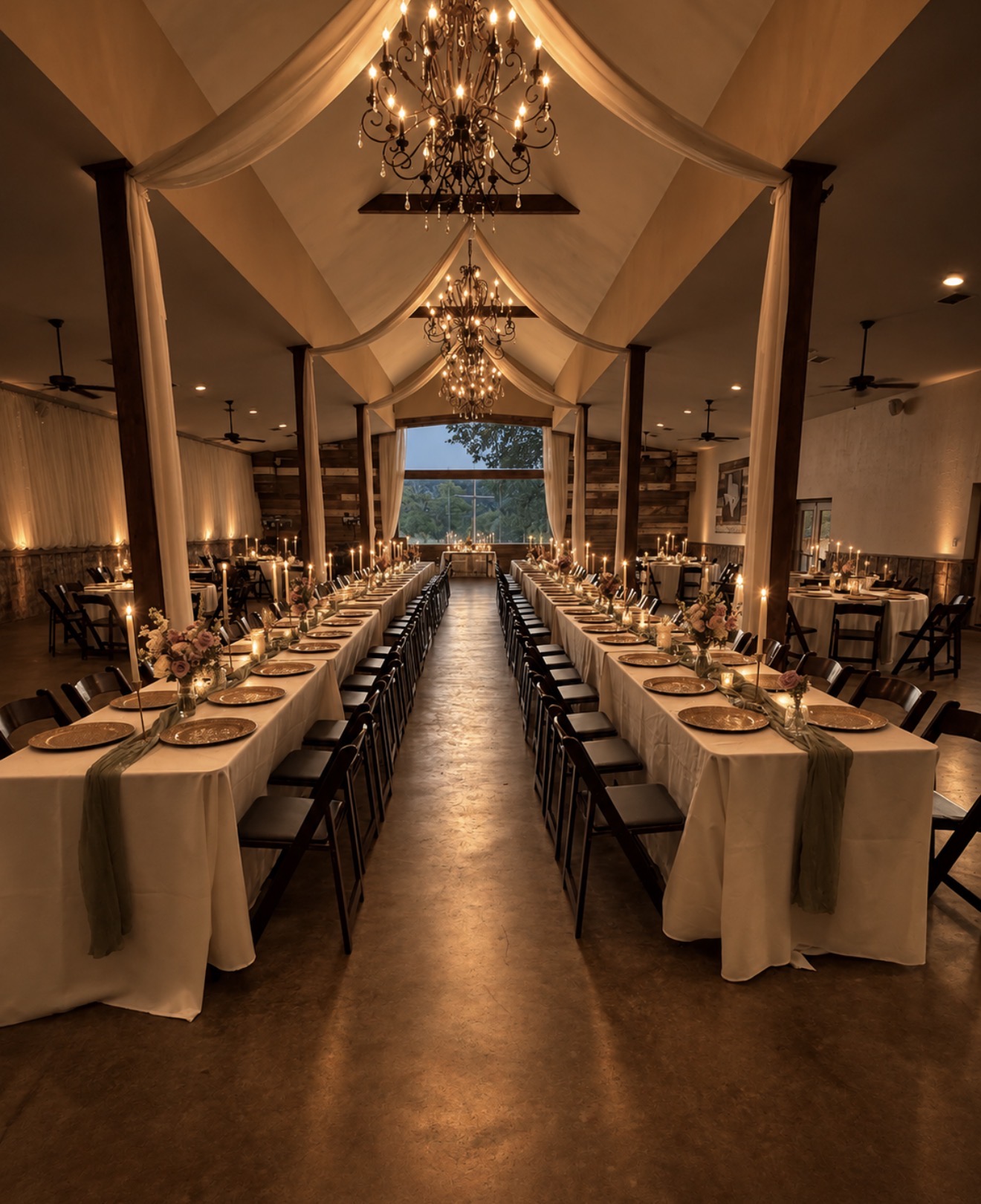 Elegant banquet hall with long tables, chandeliers, draped ceiling, and a view through large windows, set for a formal event.