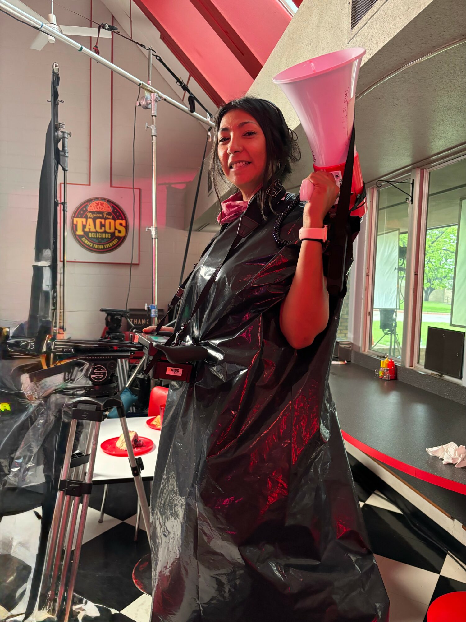Woman holding a pink megaphone inside a room with checkered floor and a Taco Bell sign, smiling at the camera.