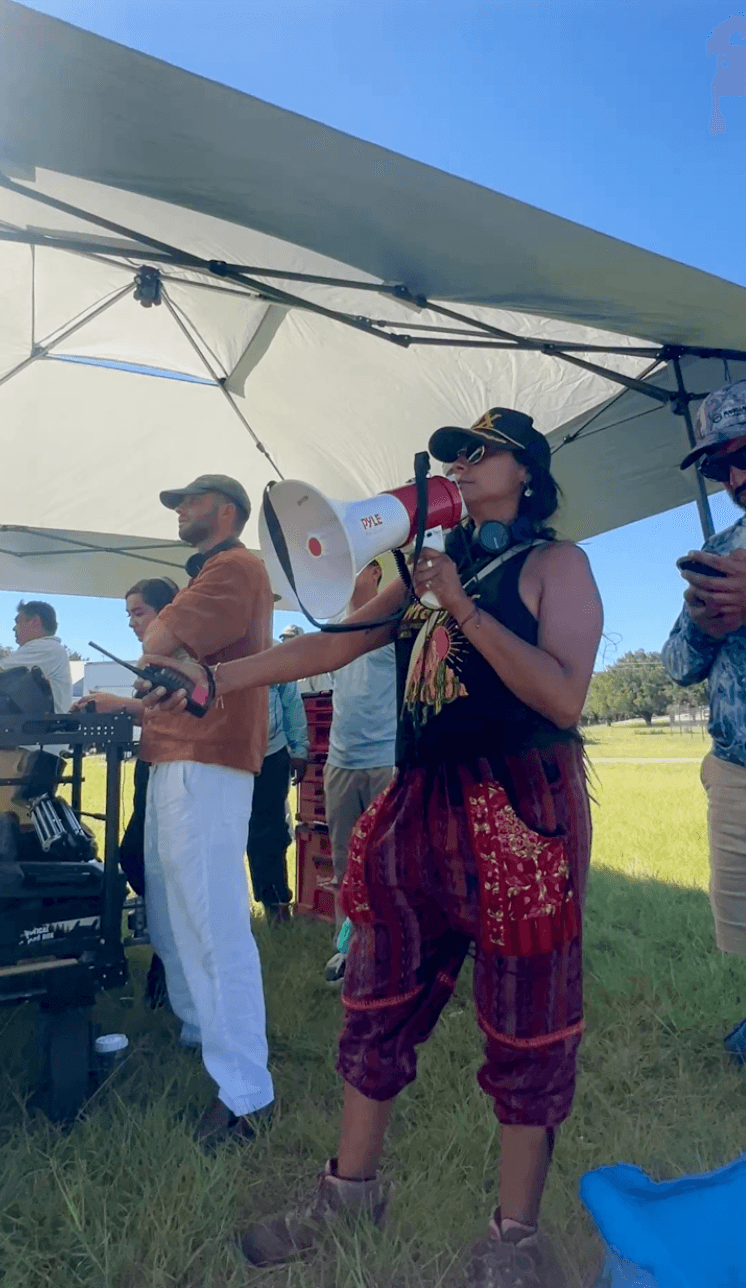 Person speaking into a megaphone at an outdoor event under a tent, with others in the background.