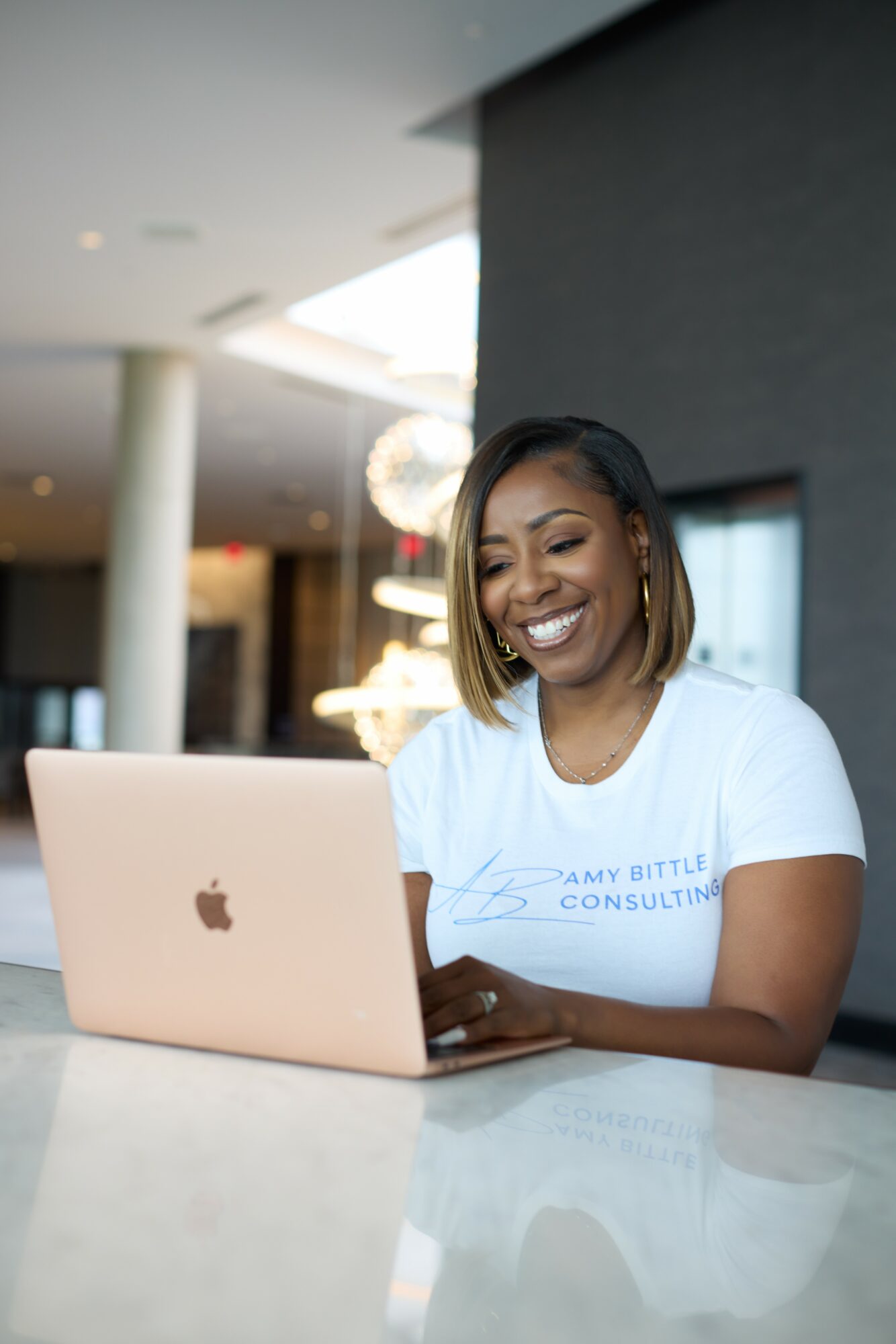 Smiling woman with shoulder-length hair working on a laptop in a modern indoor space.