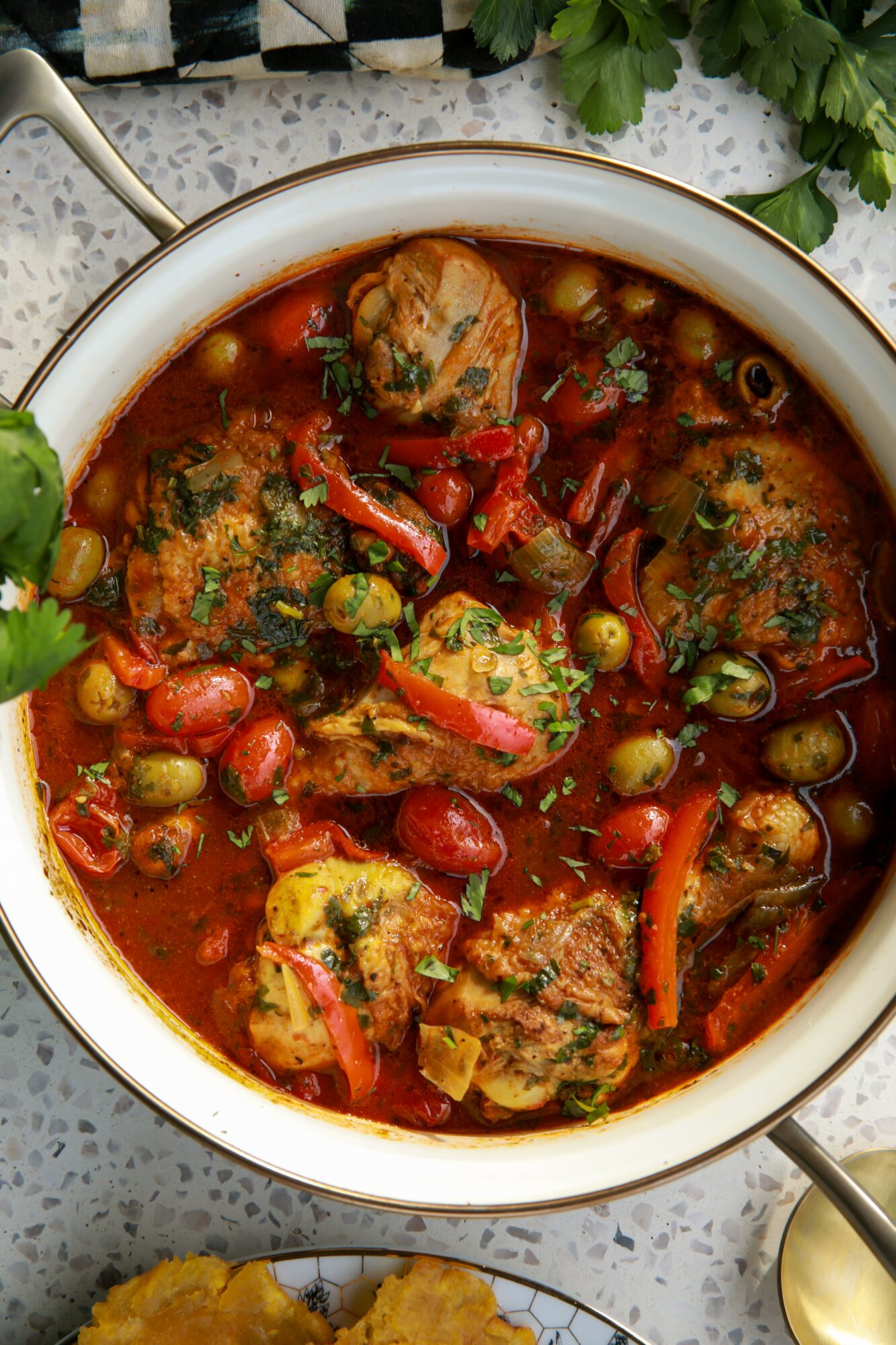 Bowl of meatballs in tomato-based soup with vegetables and herbs, garnished with cilantro, on a speckled surface with green leaves nearby.