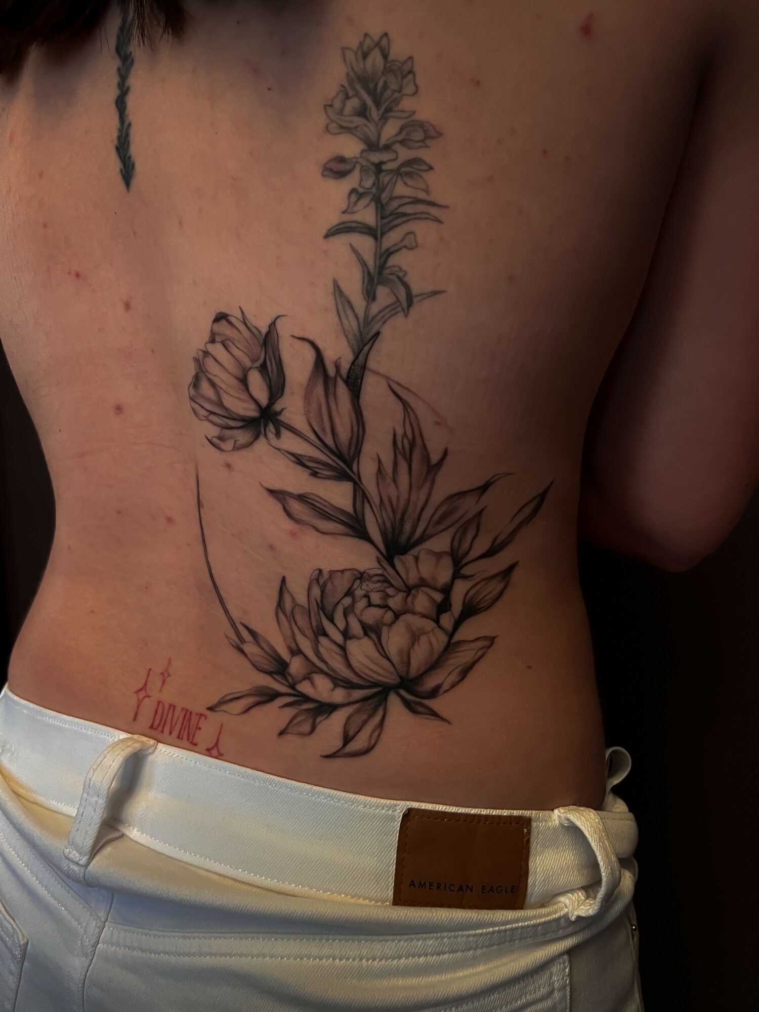 Black and gray floral tattoo on person's side, featuring a tall flower and a large blooming flower below, with leaves.