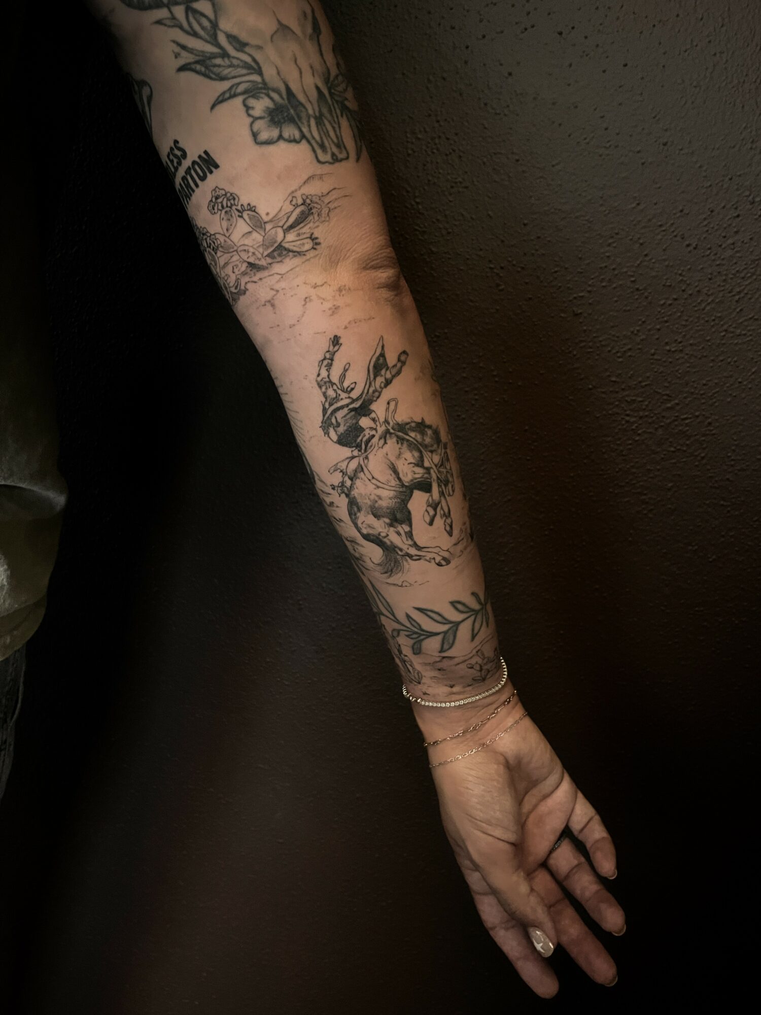 Person's arm with tattoos, including a deer and floral designs, extended downward against a dark background.