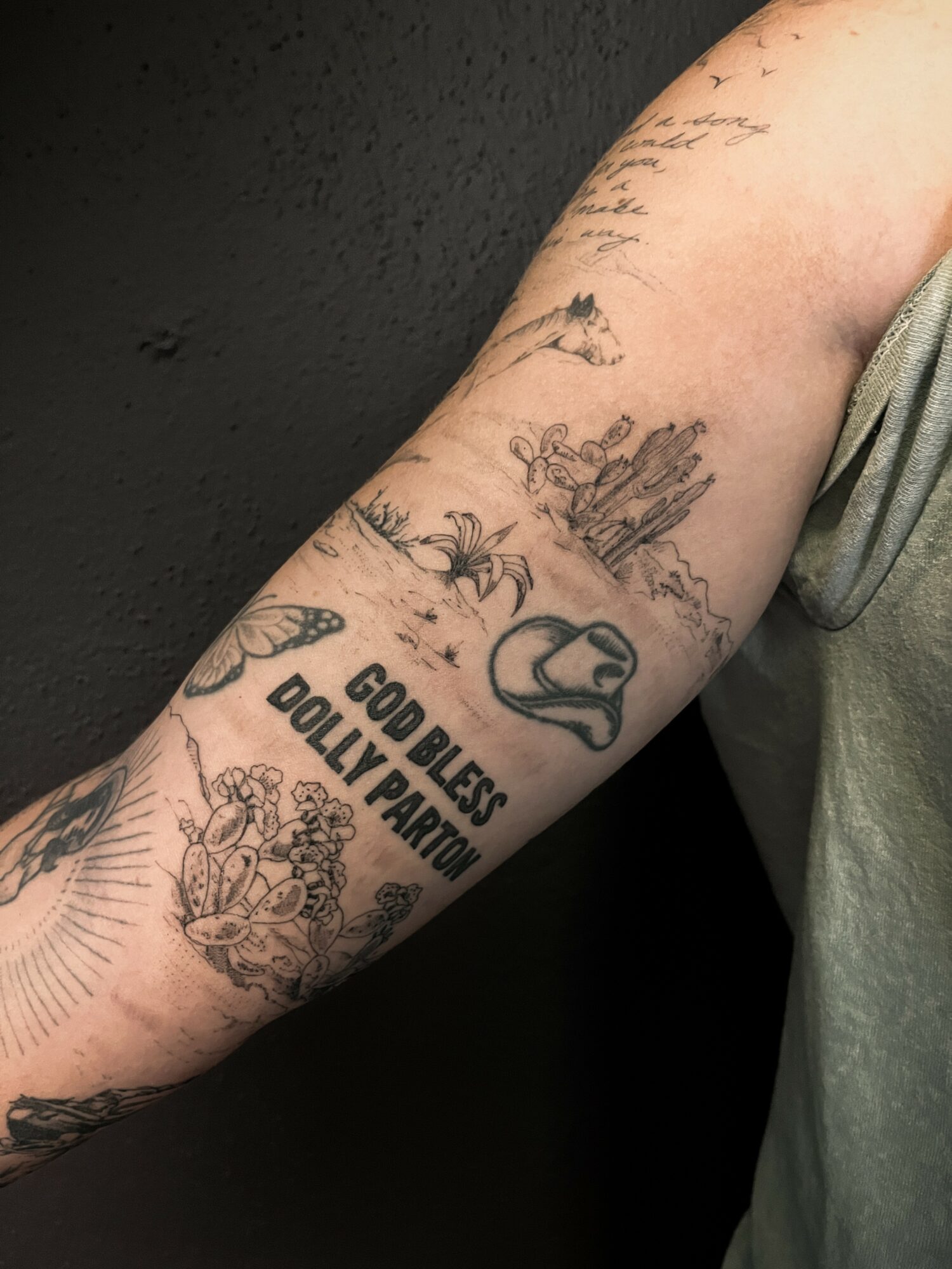 Tattooed arm with various designs, including a snake, flowers, and text reading 'Godless Dolly Parton'.