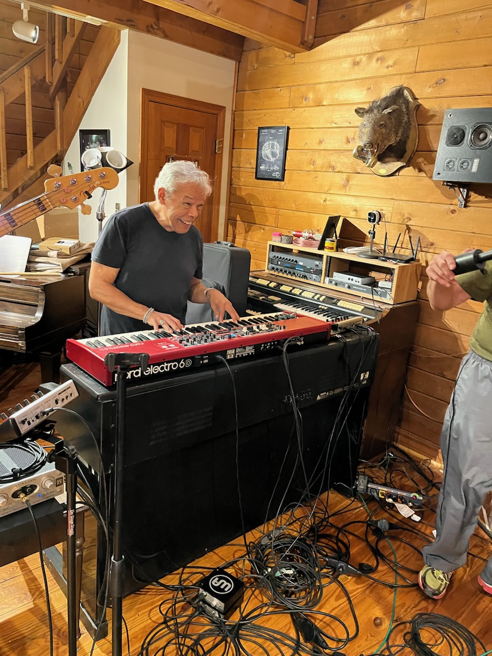Group of people playing musical instruments in a cozy wooden room, with a mounted animal head on the wall.