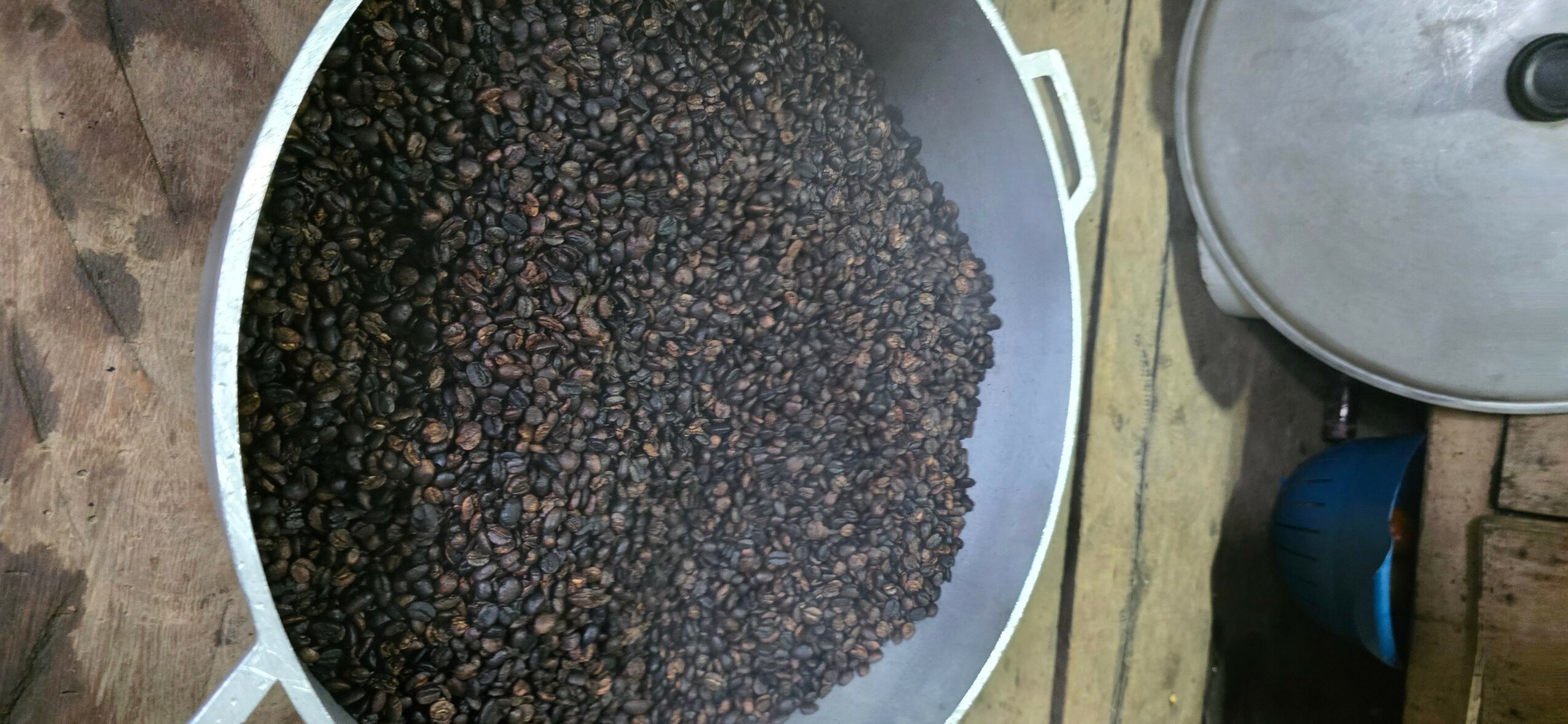 Black peppercorns in a large white container, viewed from above, on a wooden surface.