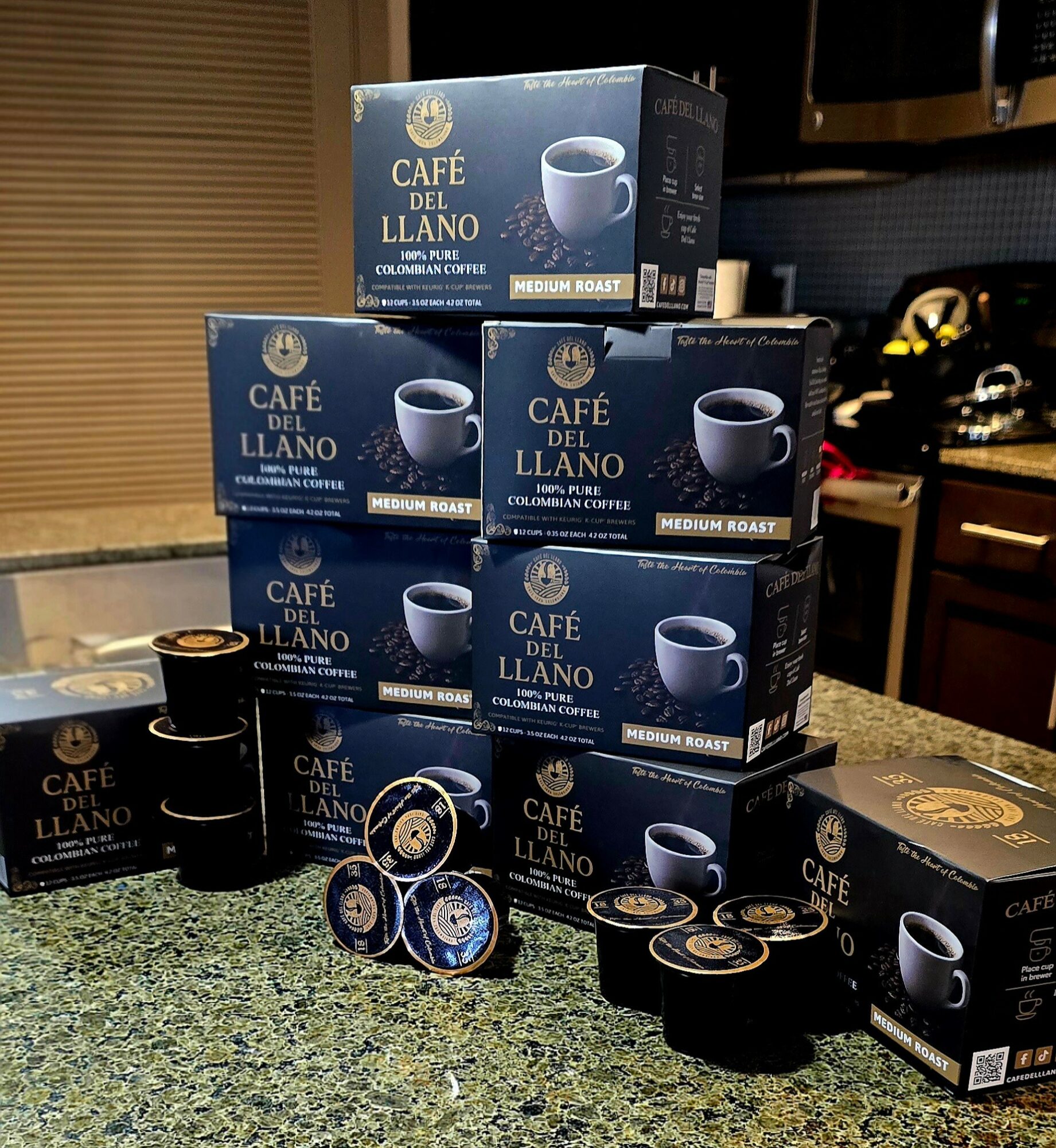 Stacked boxes of Café del Llano coffee capsules on a kitchen countertop with coffee mugs and capsules in front.