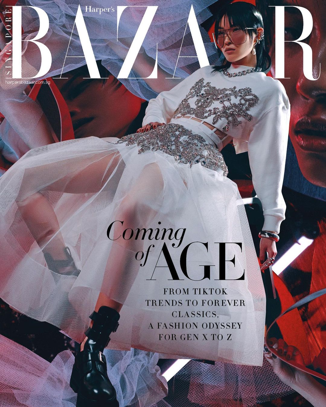 Woman in white dress with black boots sitting on a red surface, magazine cover with text and images in background.