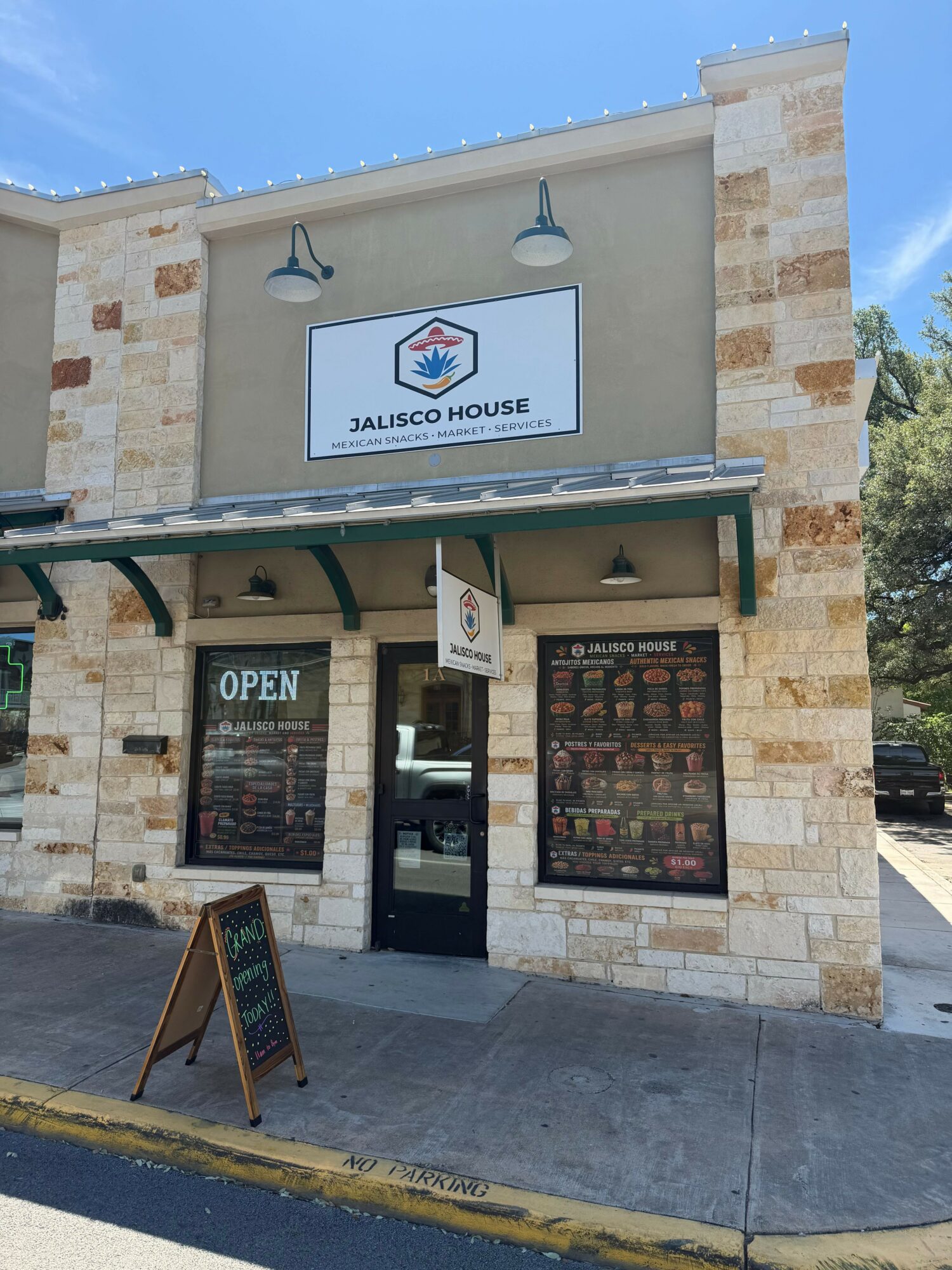 Store entrance with sign, glass door, and brick facade, with sidewalk and a small chalkboard sign outside.
